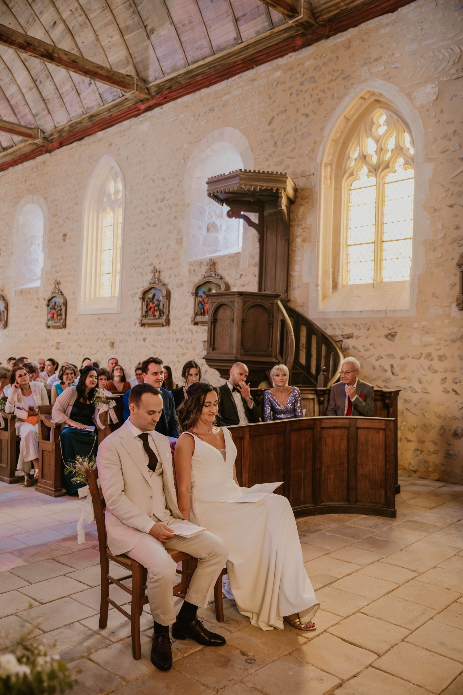 Bride and groom sit together at the altar during their church wedding ceremony with guests seated behind them.