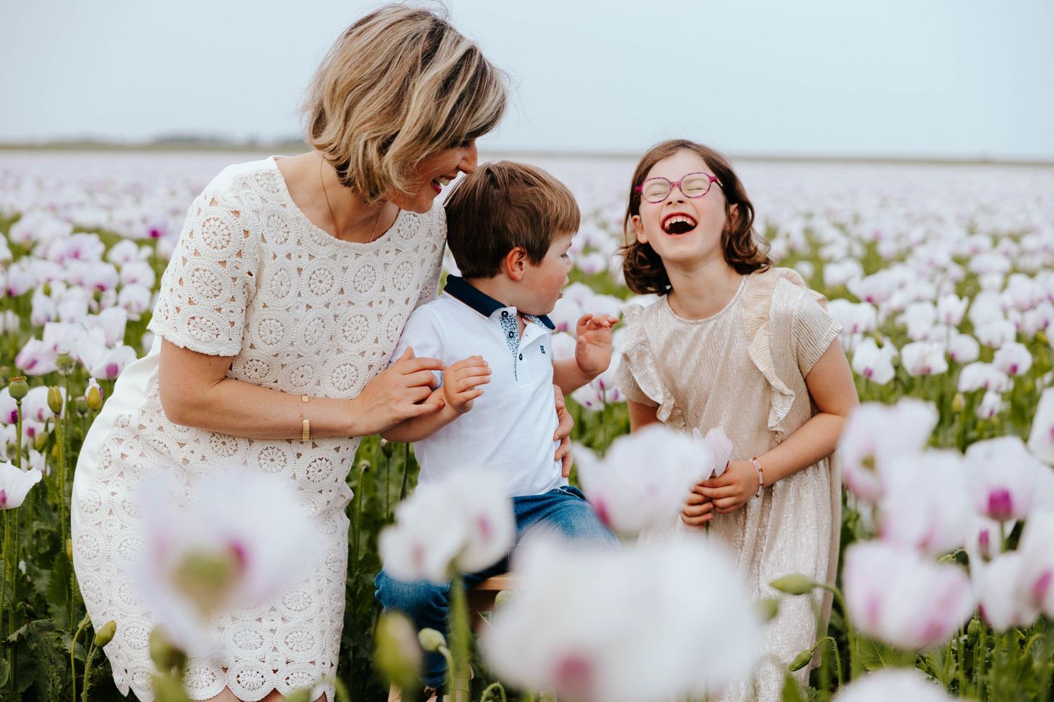 Grandmother laughing with grandchildren in a stunning field of white and pink poppies.