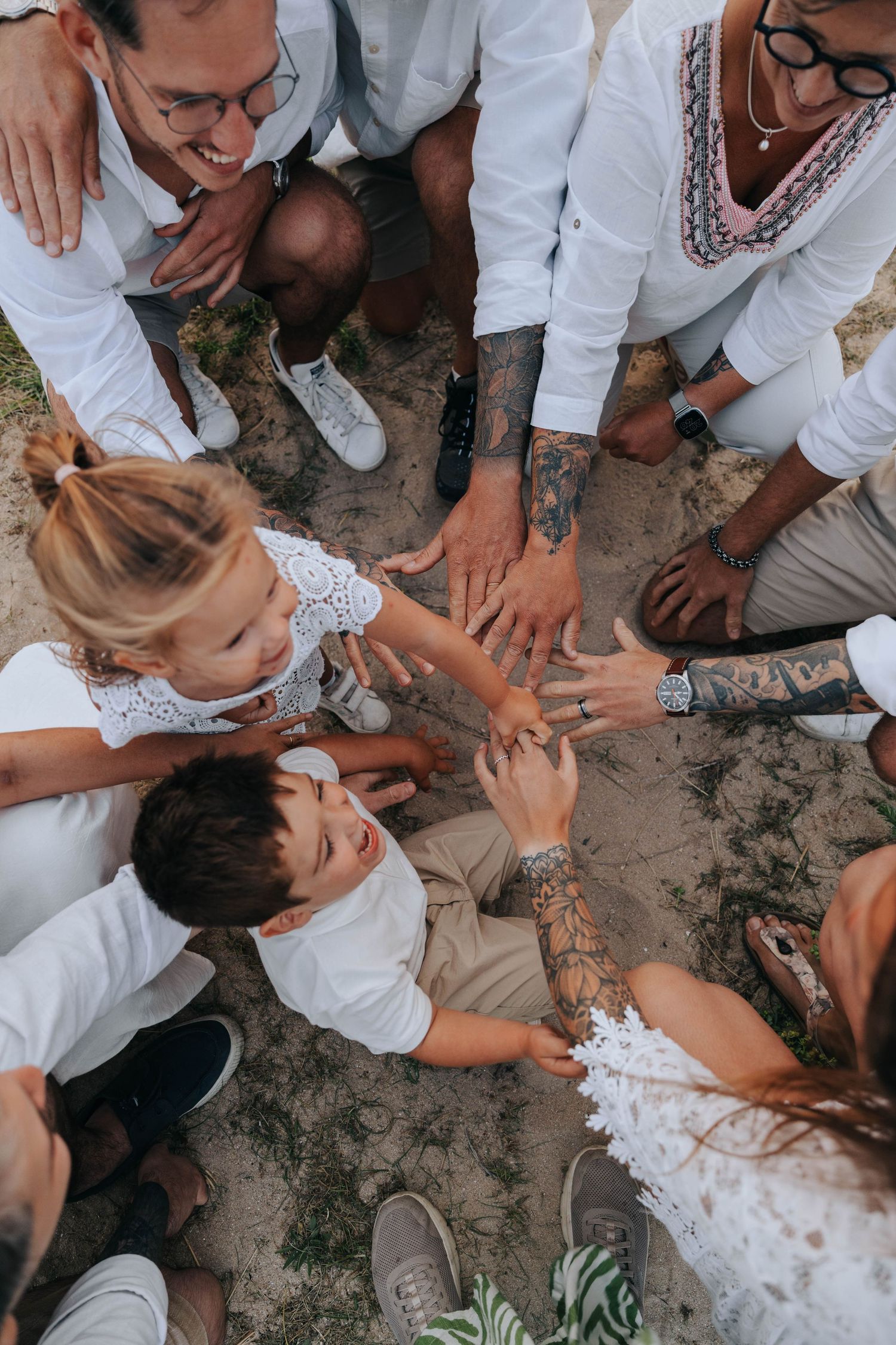 Overhead view of family in white outfits joining hands together in a circle on sand.