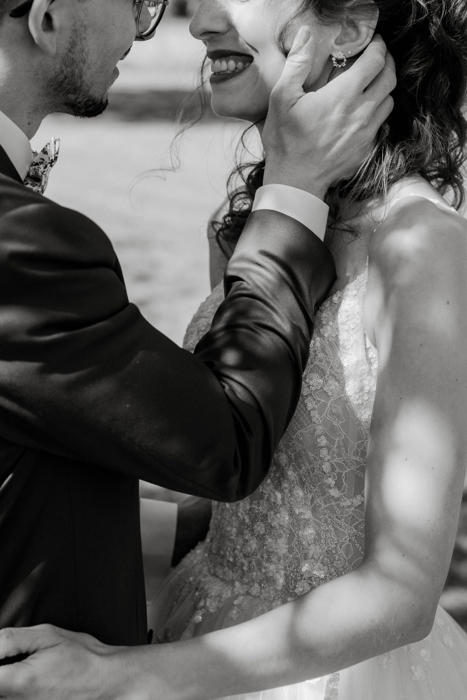 Black and white photo of groom tenderly cupping brides face during romantic wedding moment.