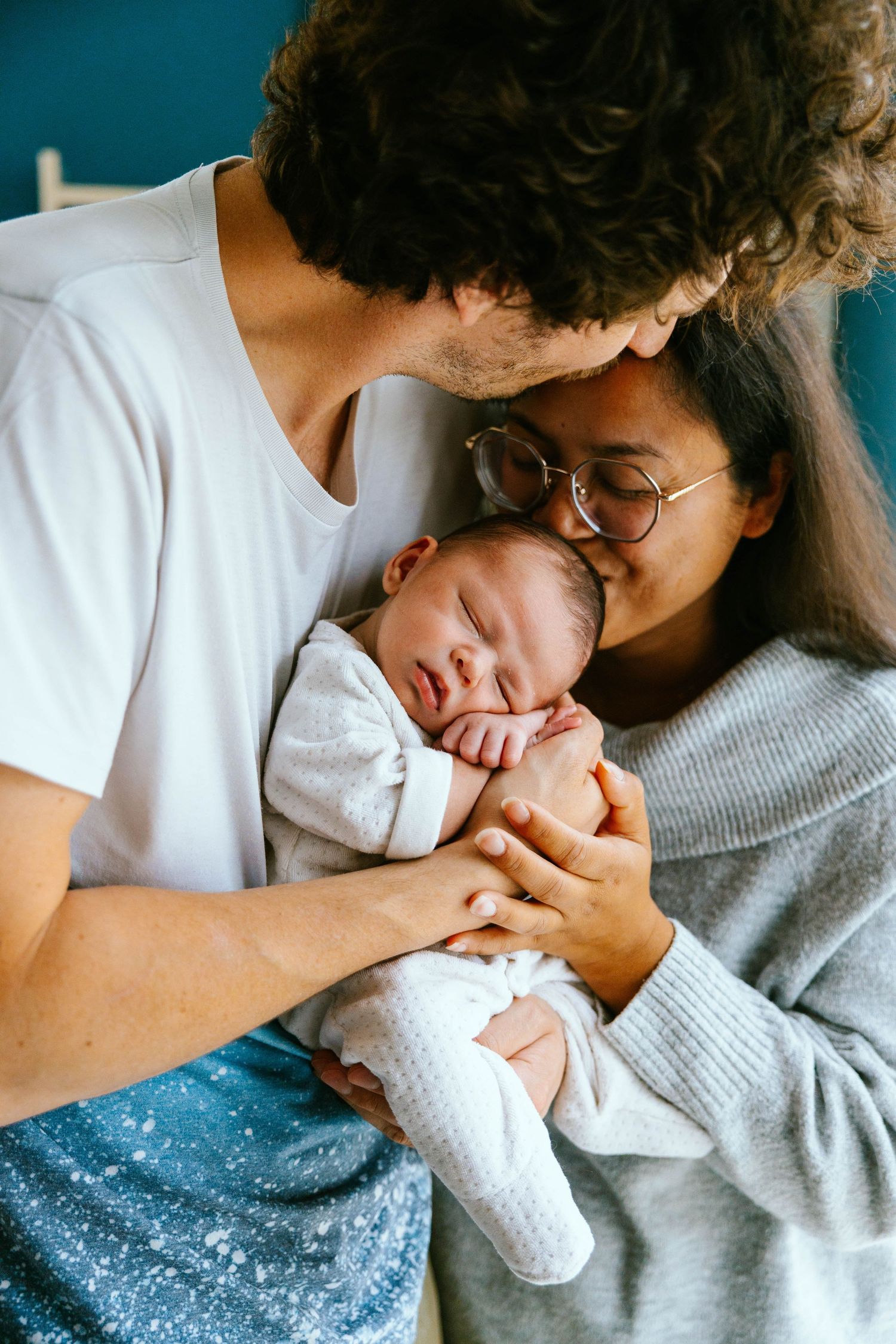 Loving interracial parents kissing their sleeping newborn baby together.