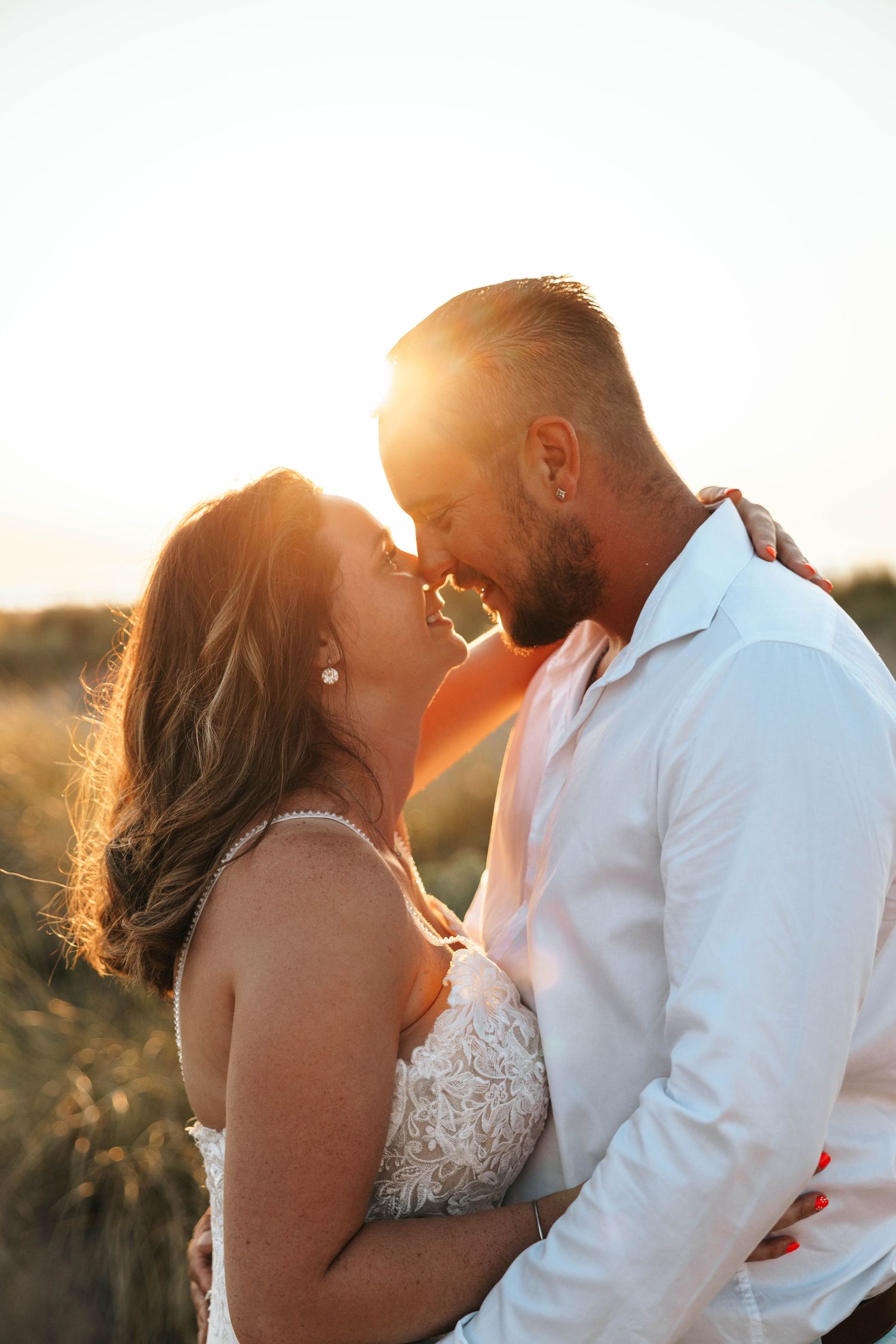 Bride and groom sharing a romantic almost-kiss at golden hour sunset in an outdoor field.