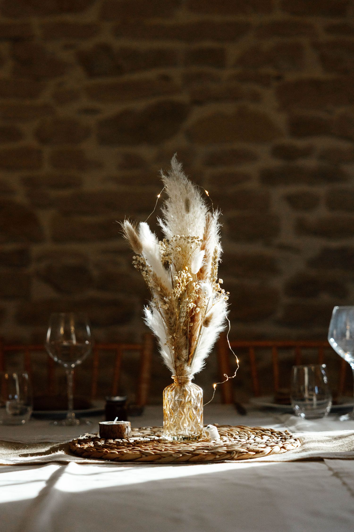 Elegant dried pampas grass centerpiece in a glass vase on a rustic wedding reception table setting.