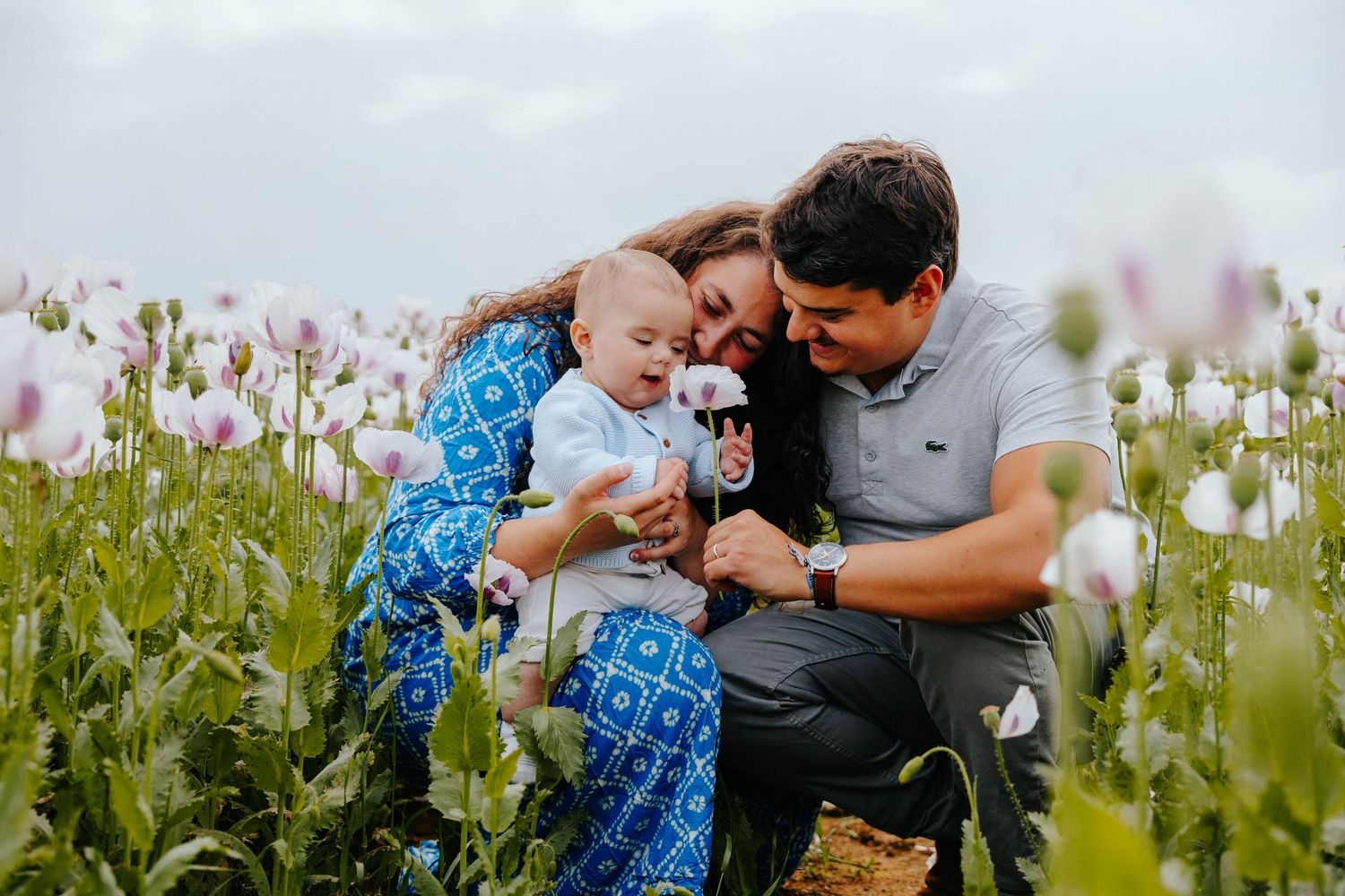 Young couple with baby in a beautiful field of pink and white poppy flowers outdoors.