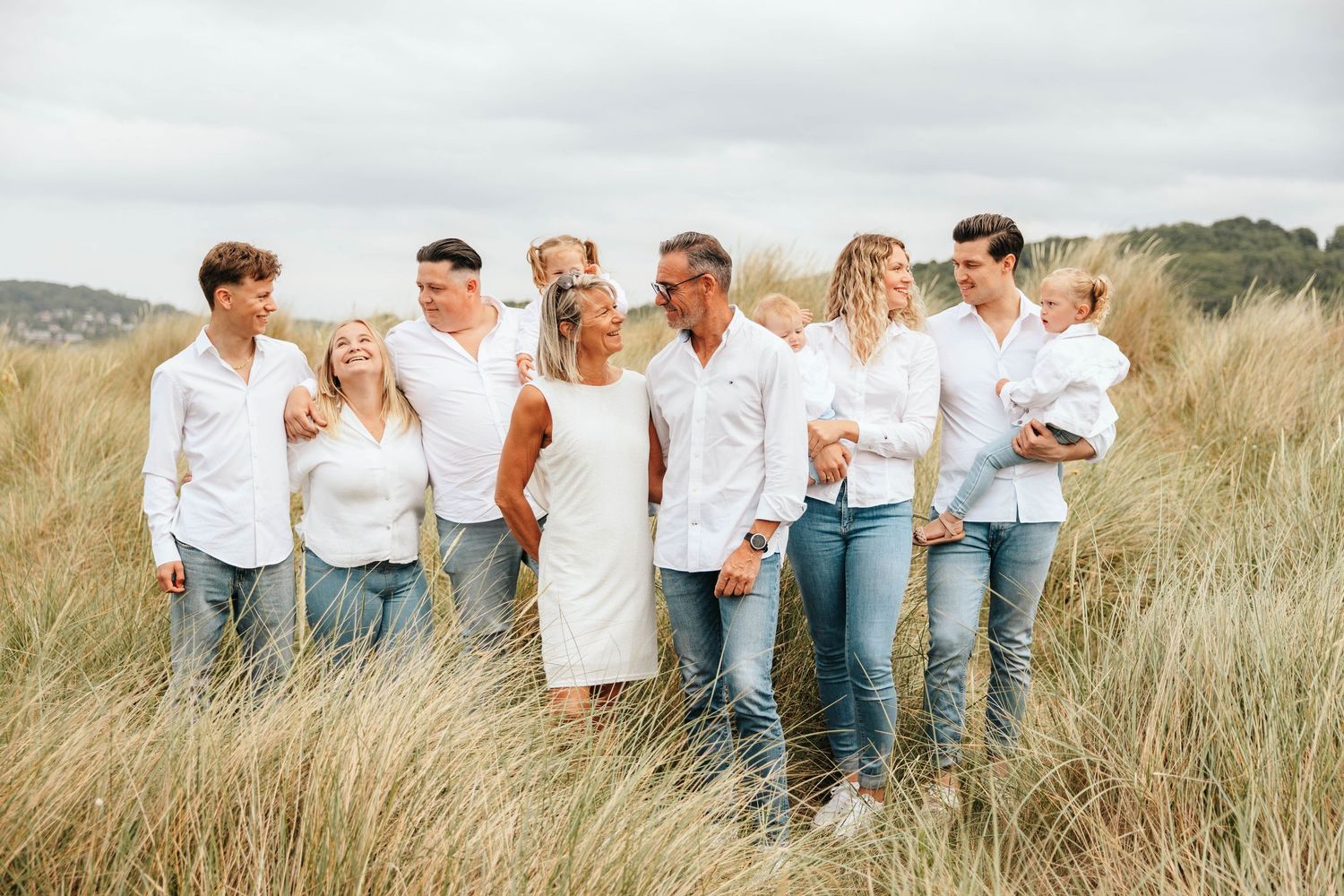 Family of eight in white shirts and jeans posing together in tall coastal grass dunes.