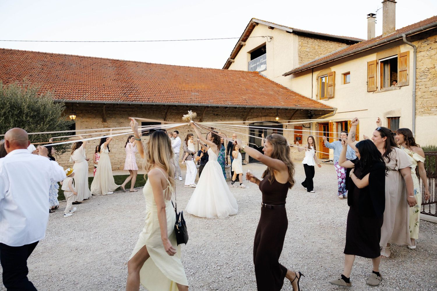 Wedding guests celebrating outdoors at a rustic venue, with bride in white gown joining the festivities.