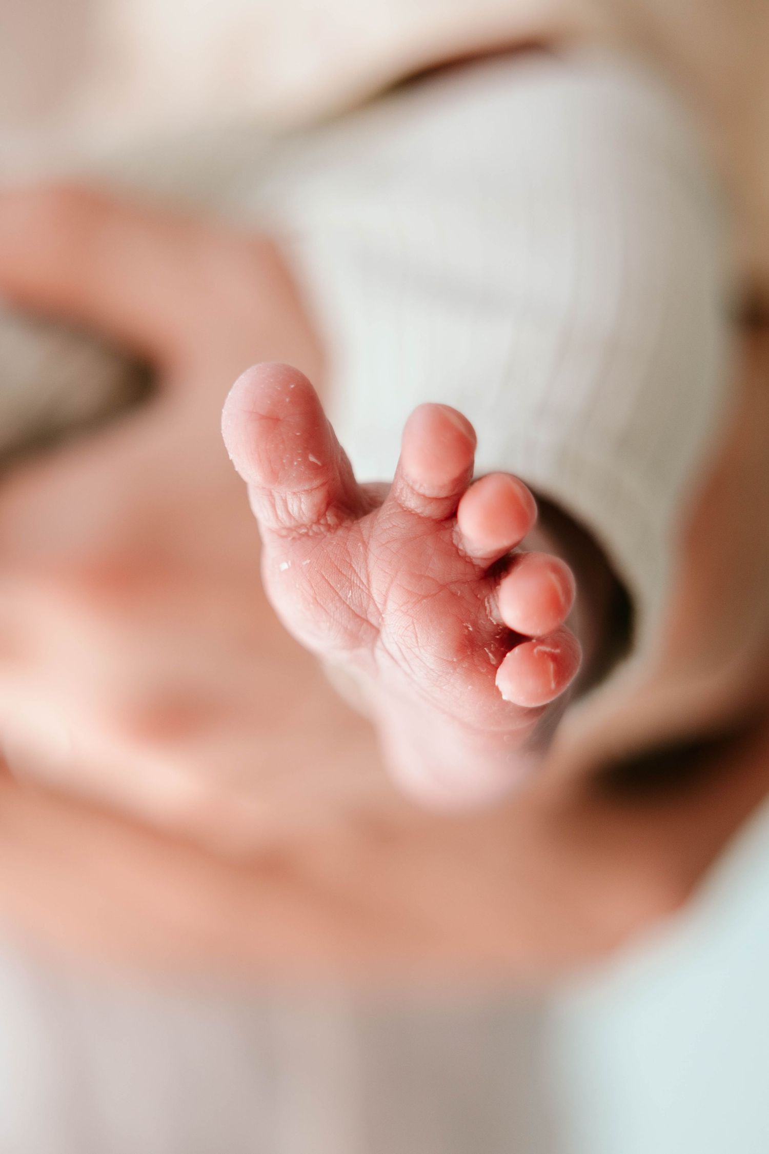 Close-up of a newborn baby's tiny foot with delicate wrinkled skin against a soft white background.