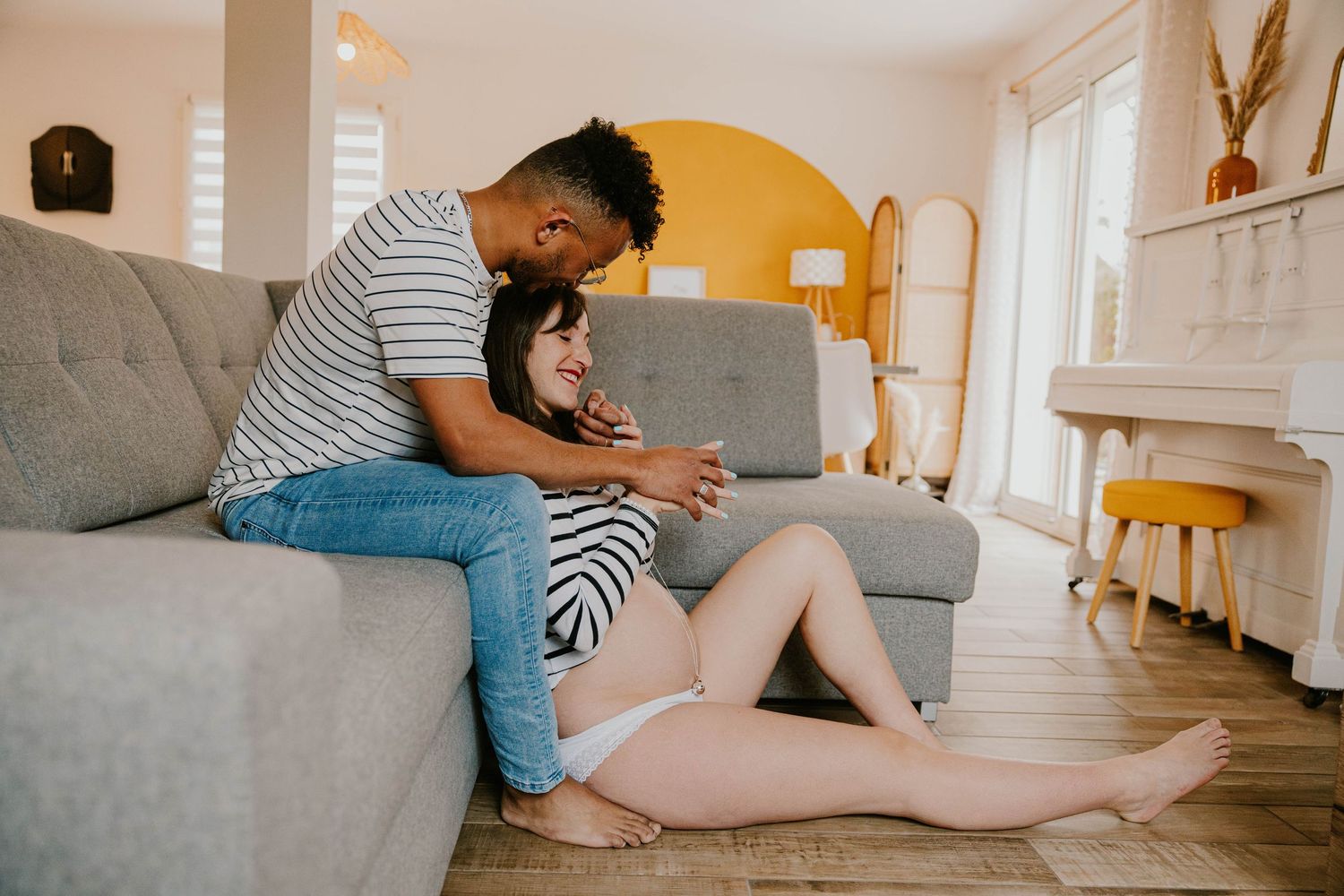 Couple relaxing at home on couch, man sitting above woman who leans against him on floor.