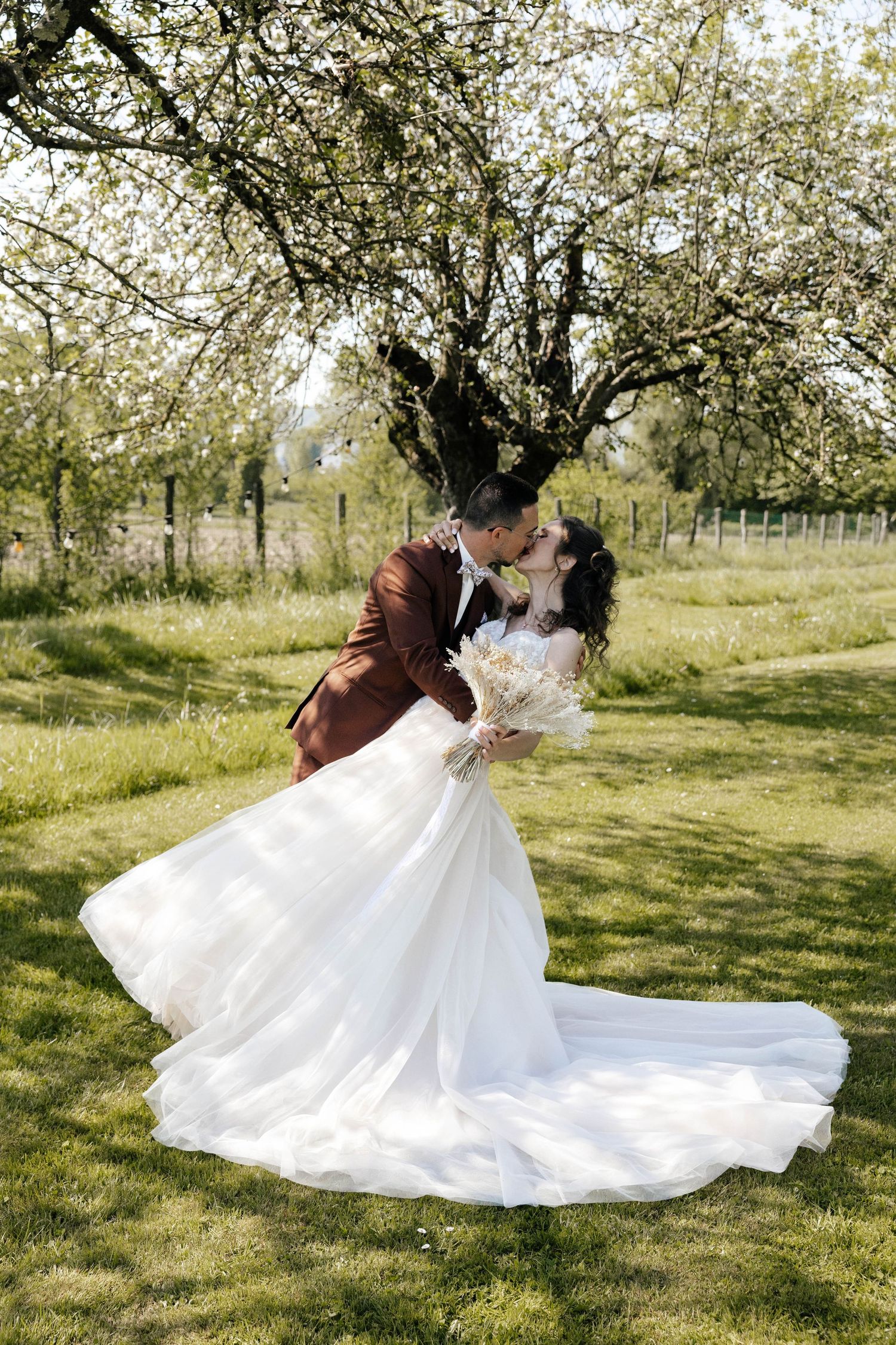 Bride and groom sharing romantic kiss under blooming tree in sunny outdoor garden.