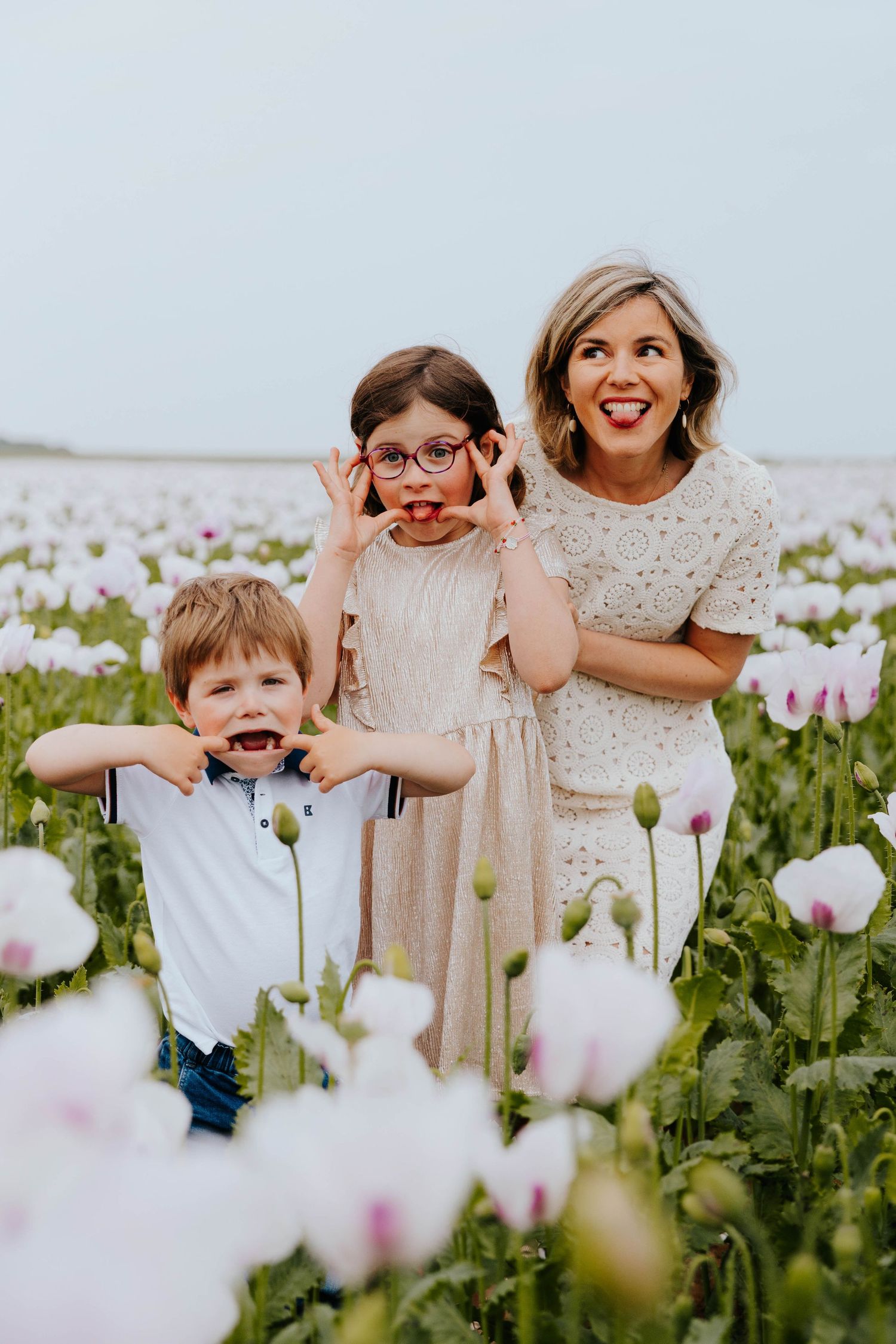 Joyful mother and two children making funny faces in a white poppy flower field.