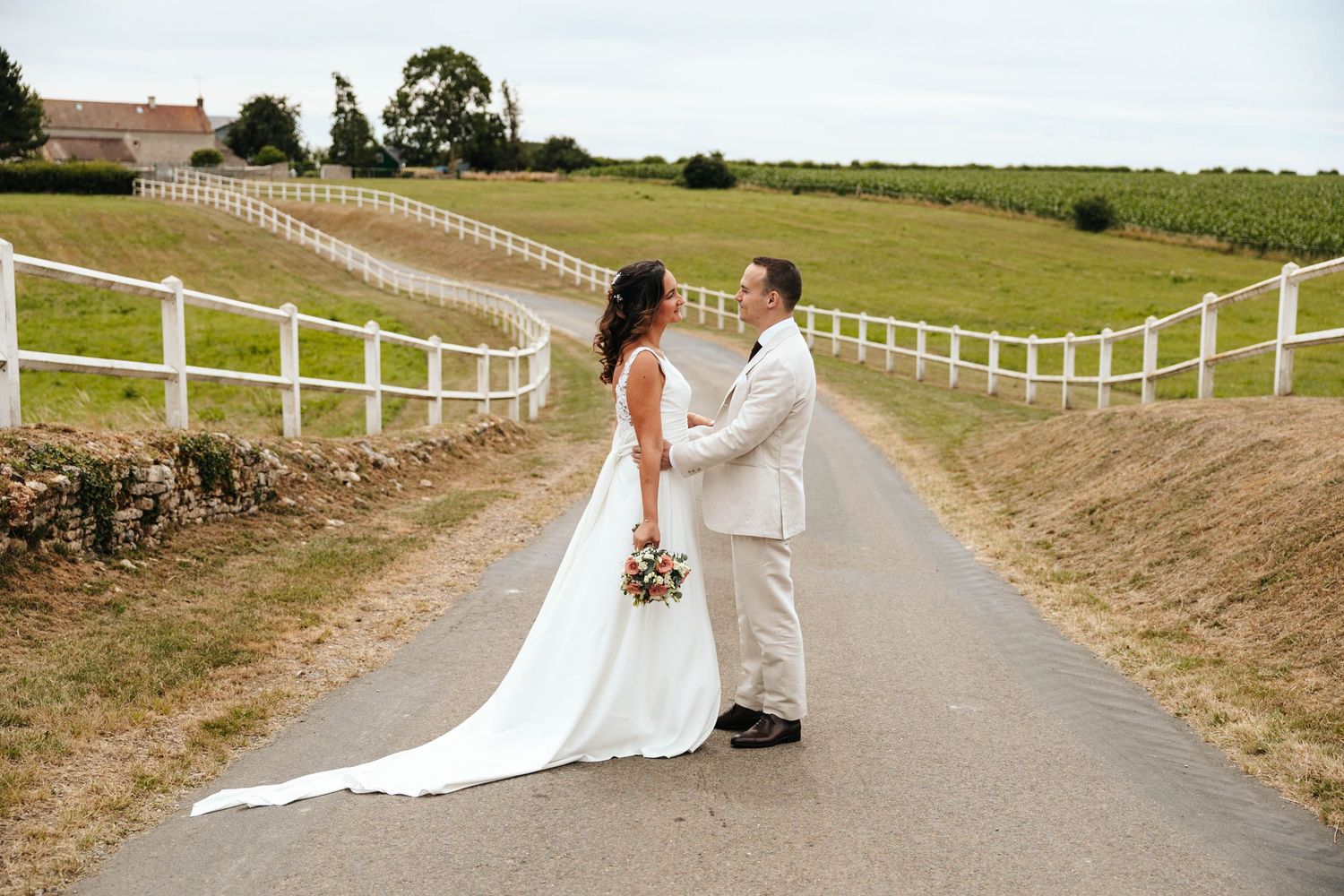 Bride and groom sharing romantic moment on scenic countryside road with rolling green hills behind them.
