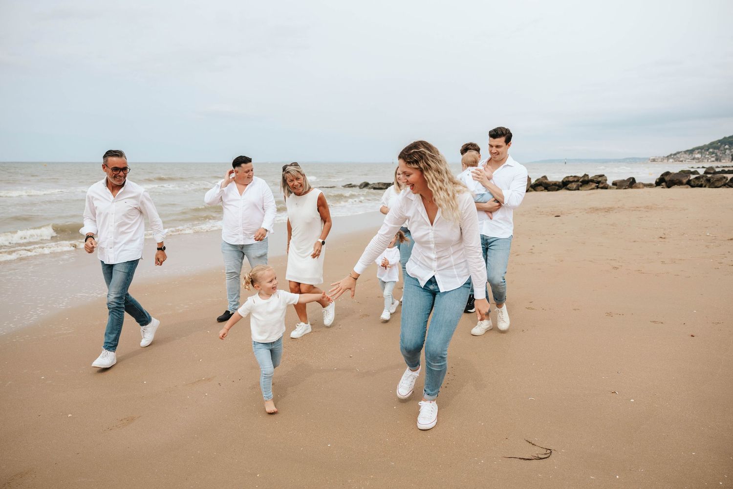 Happy family in matching white shirts running together on a sandy beach.