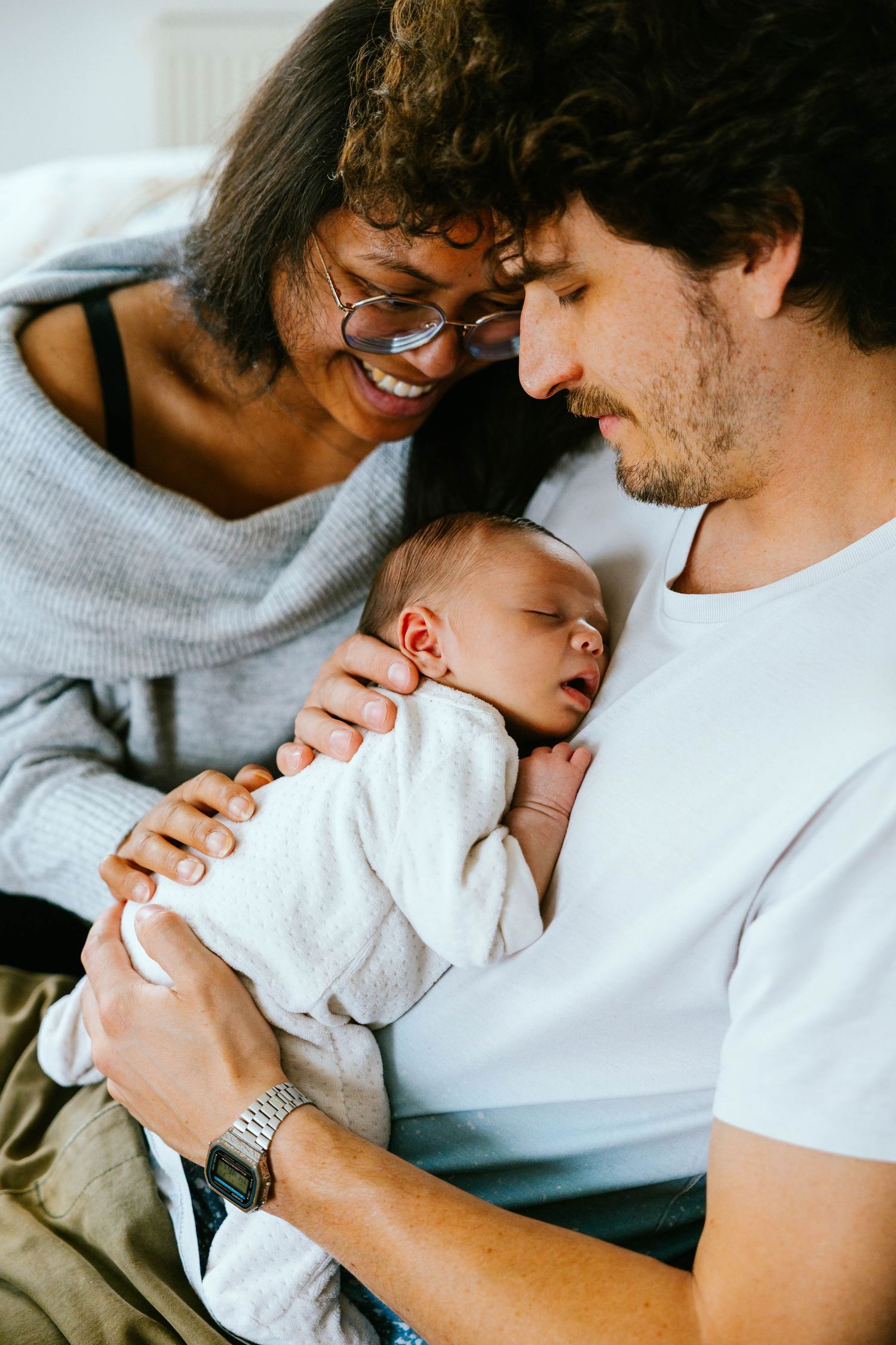 Happy interracial couple smiling at their sleeping newborn baby held in fathers arms.