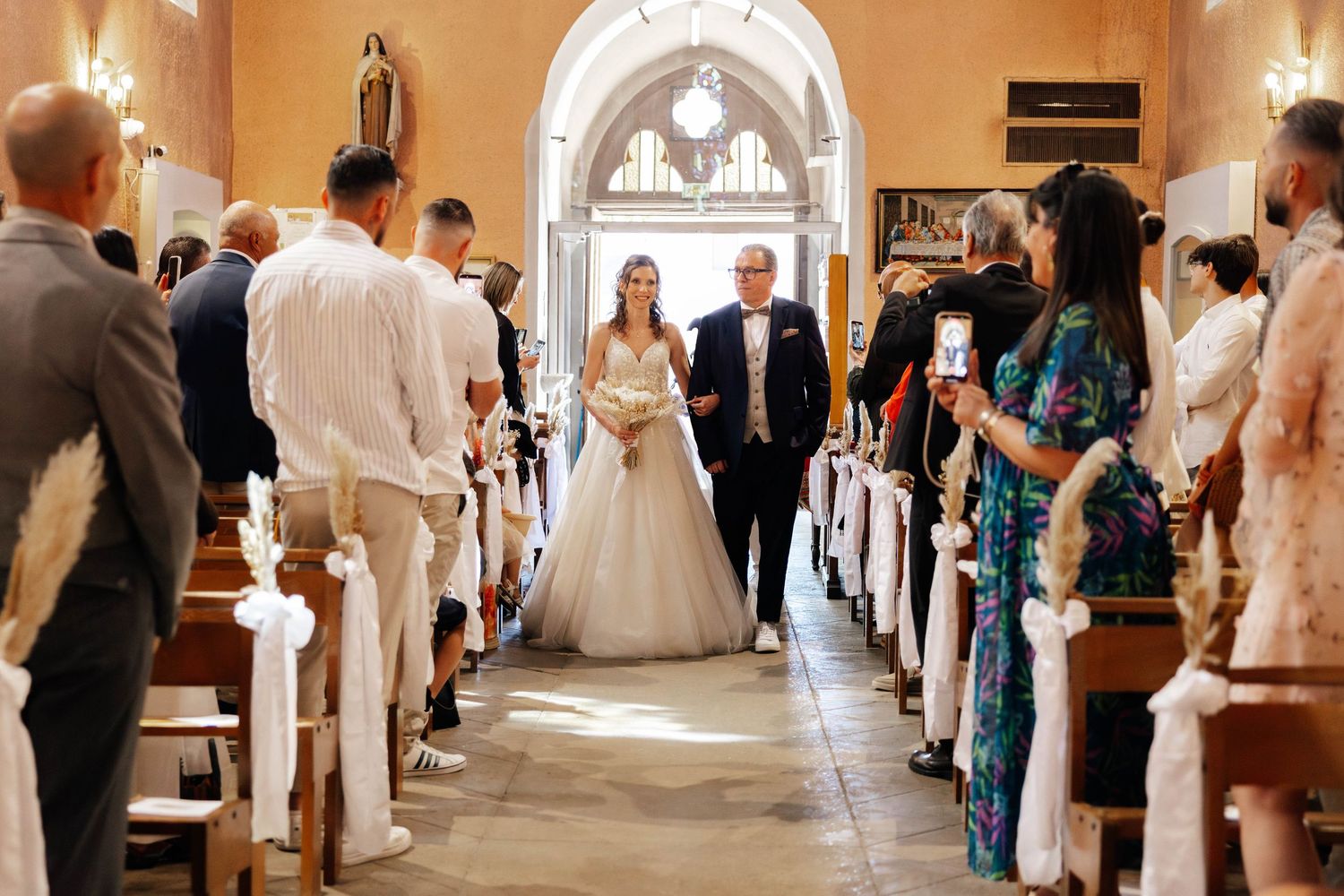 Bride walking down the church aisle with escort, guests watching on both sides.