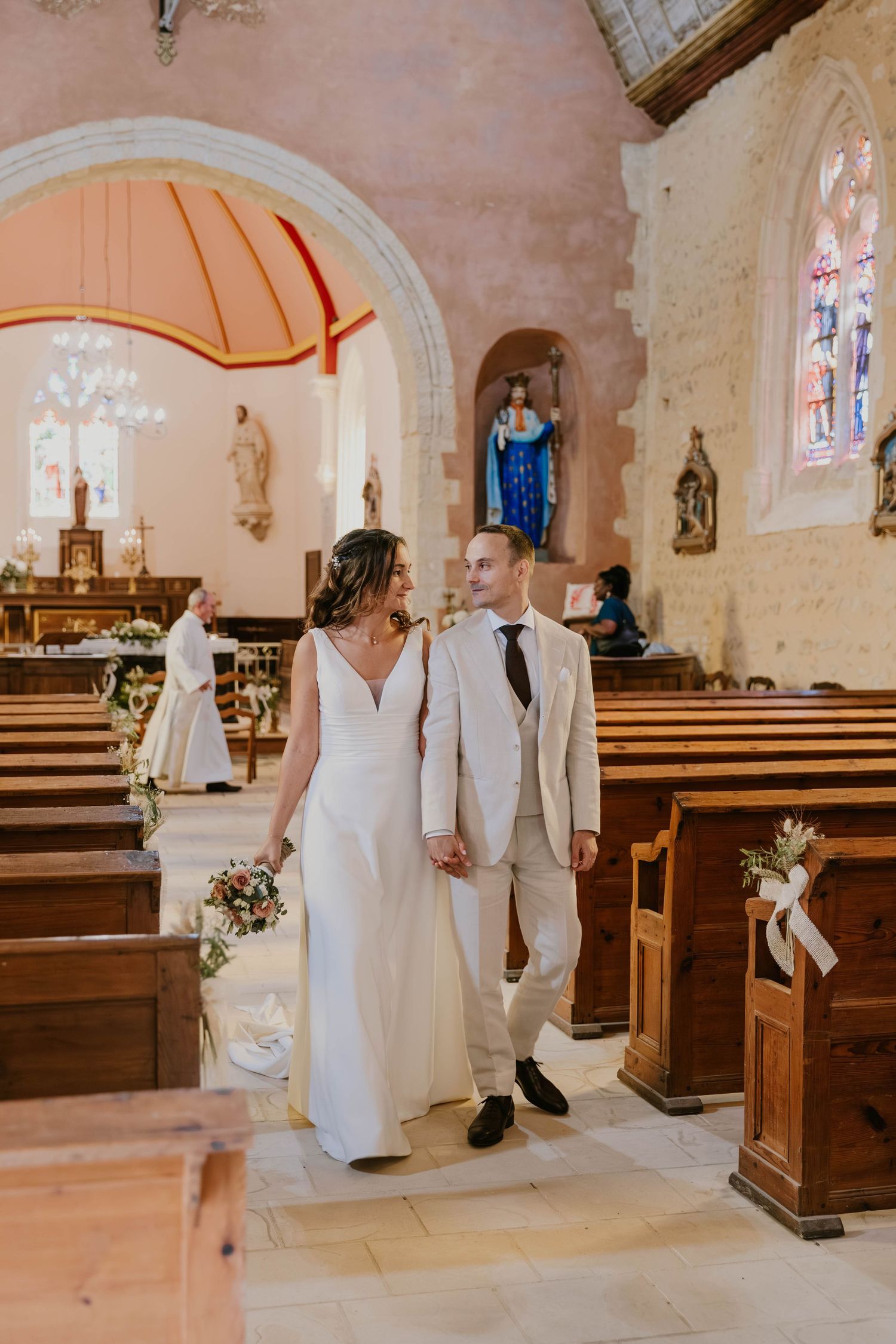 Bride and groom walk hand in hand down the aisle of a rustic stone church after their wedding ceremony.