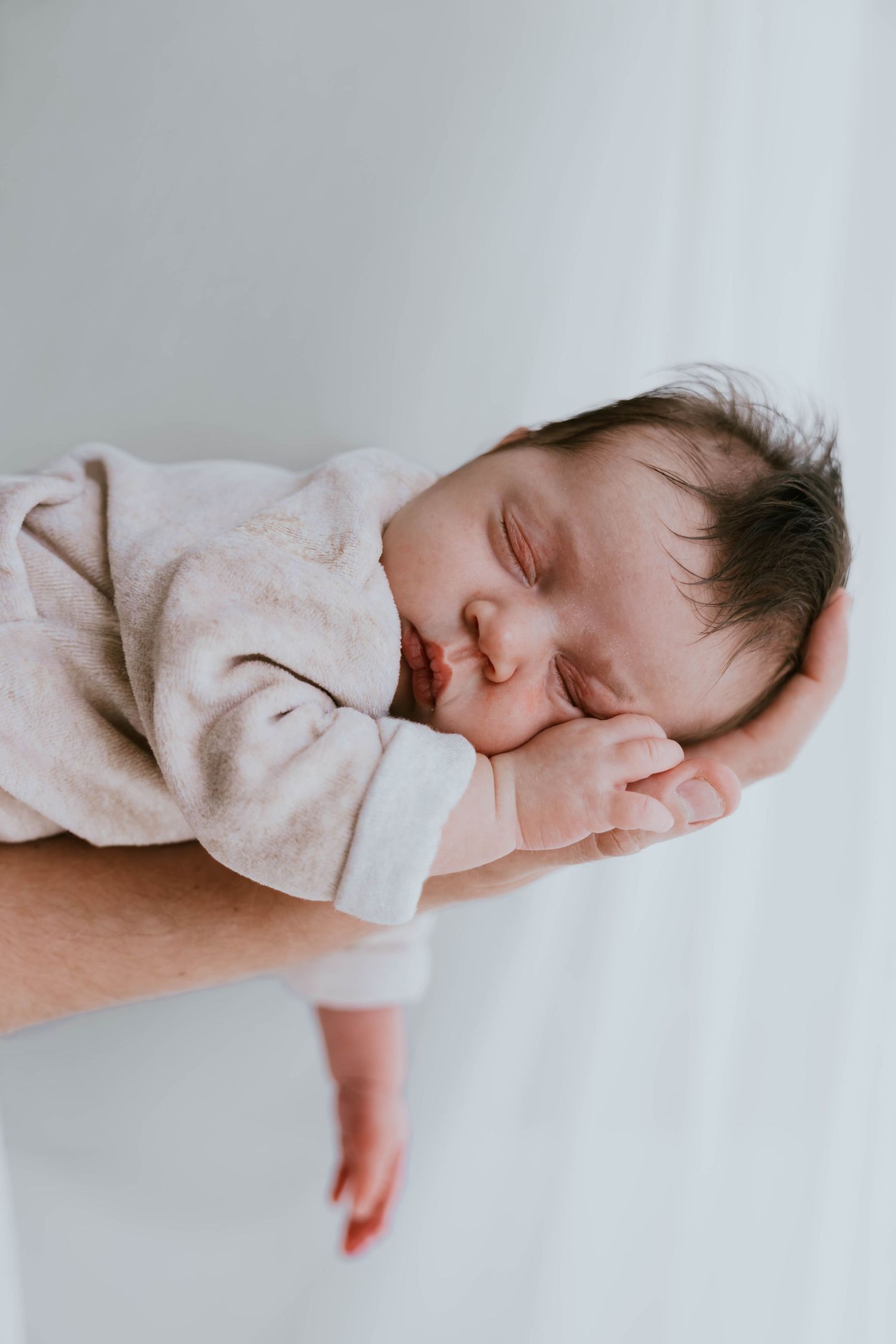 Sleeping newborn baby cradled gently in parent's supportive hand.
