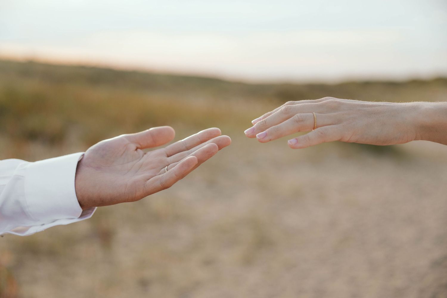Two hands reaching toward each other on a sandy beach background.