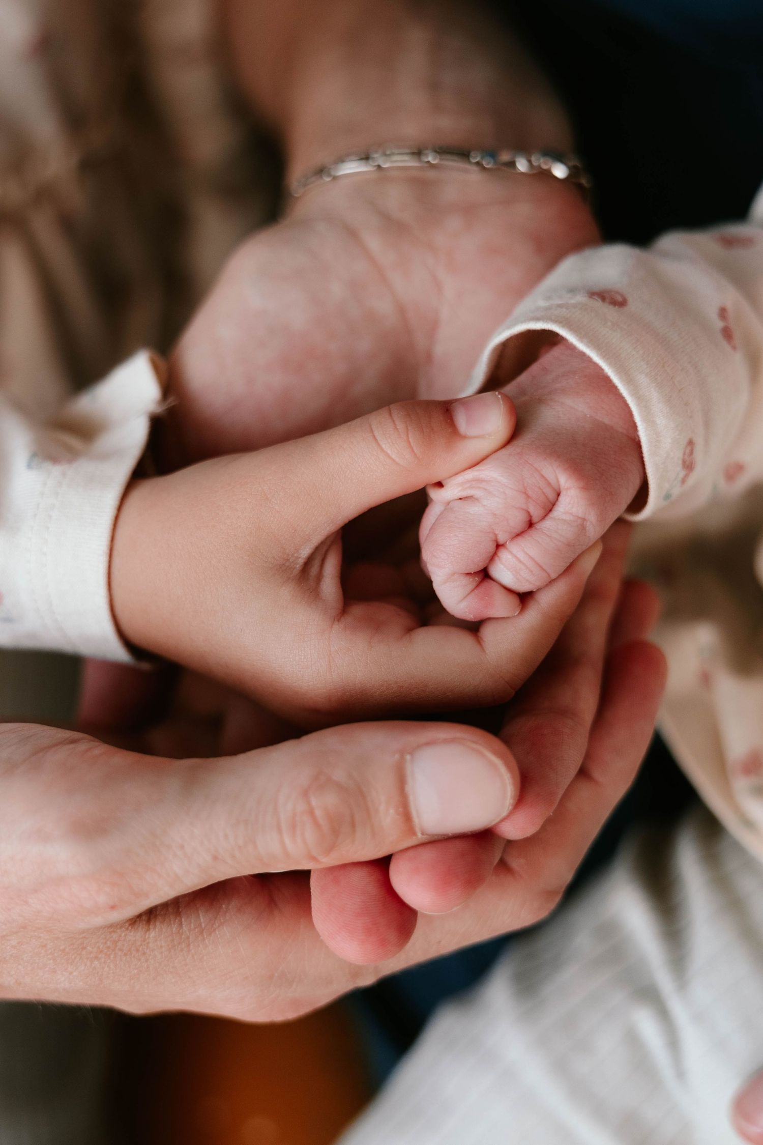 Newborn baby's tiny fist gently gripped by toddler and adult hands layered together tenderly.