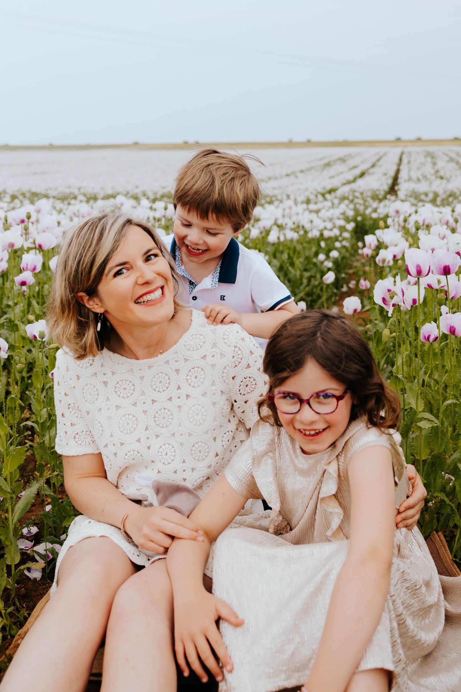 Smiling mother sitting with son and daughter wearing glasses in a purple poppy field.