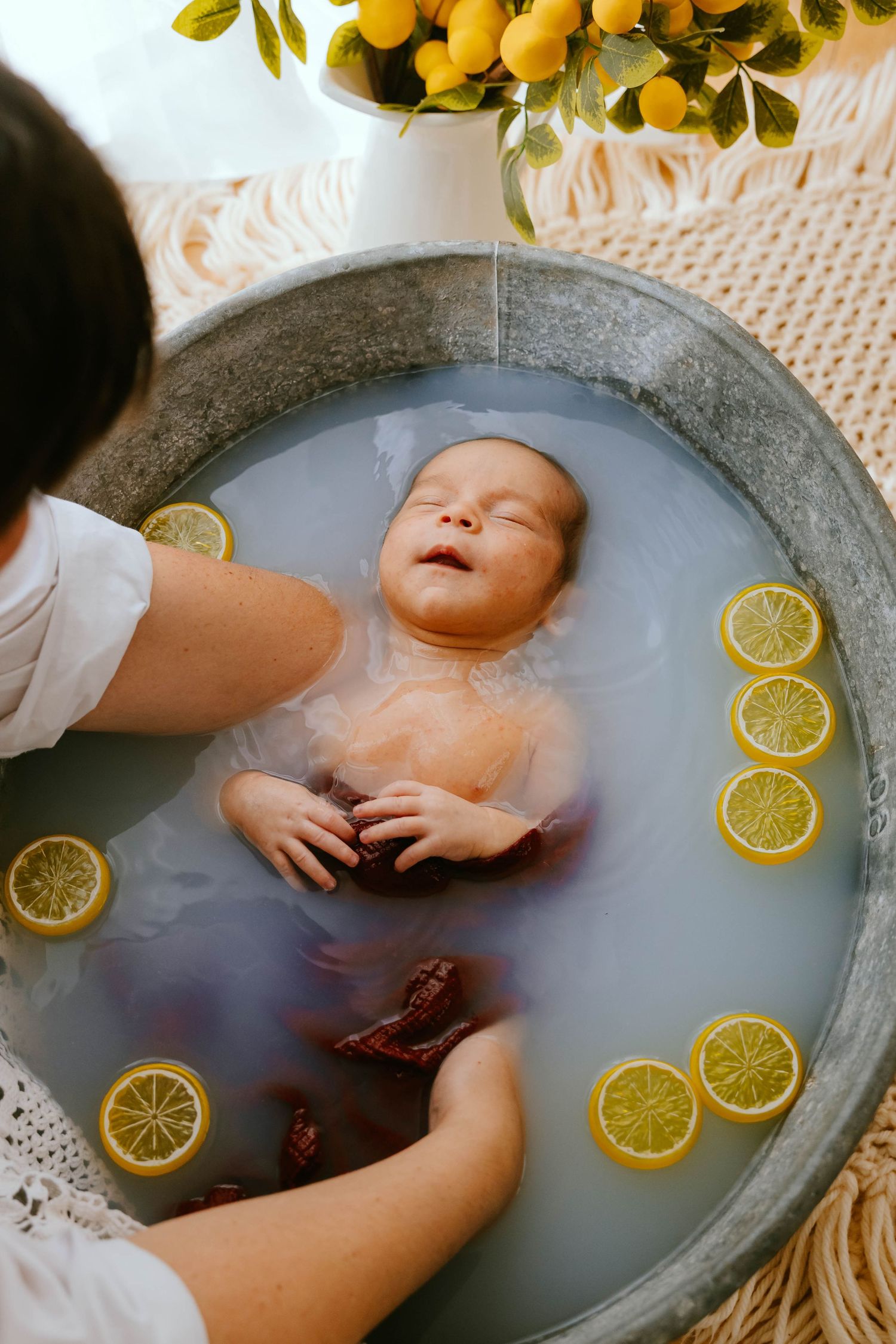 Overhead view of peaceful newborn baby floating in milk bath with lemon slices decoration.