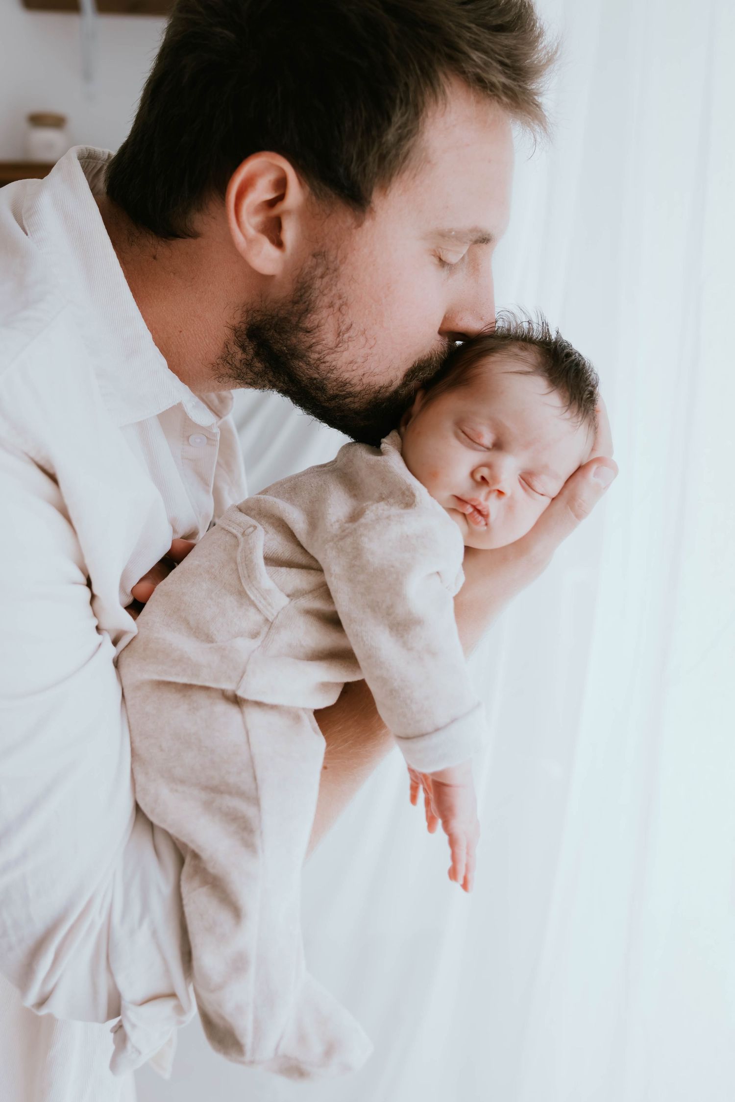 Father kissing sleeping newborn baby while holding them close to his chest.