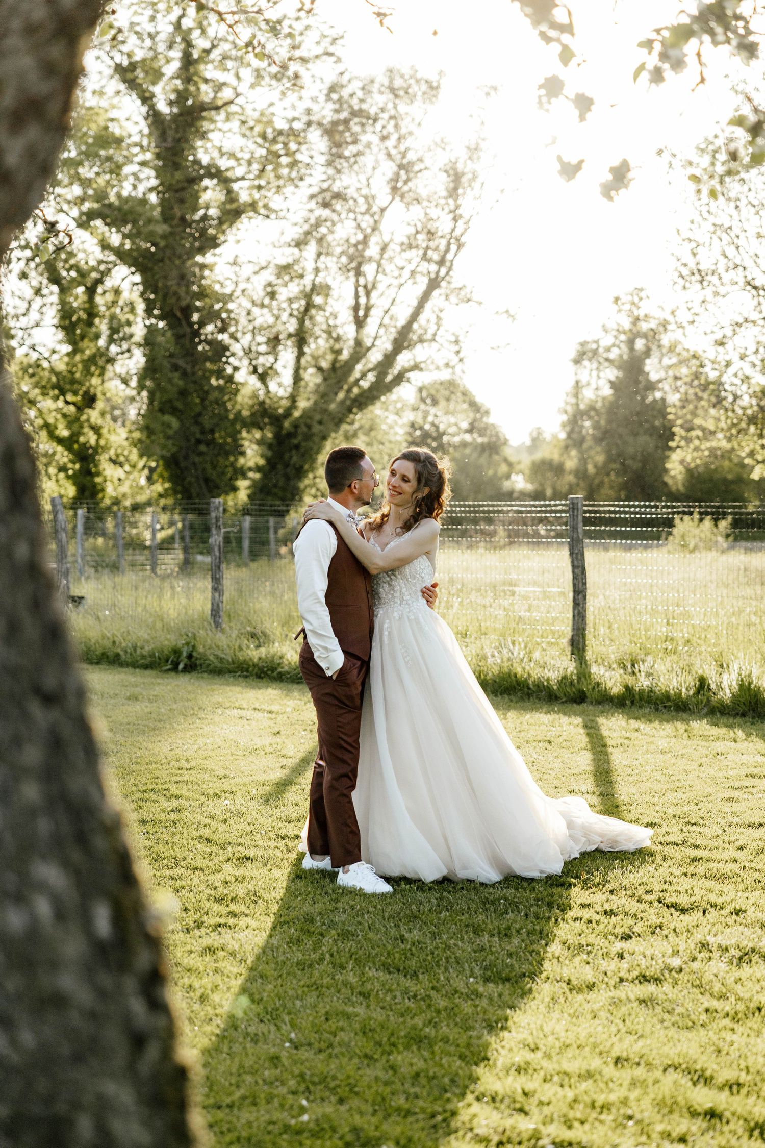 Bride and groom embrace tenderly in a sunlit garden, bride wearing a flowing white tulle wedding gown.
