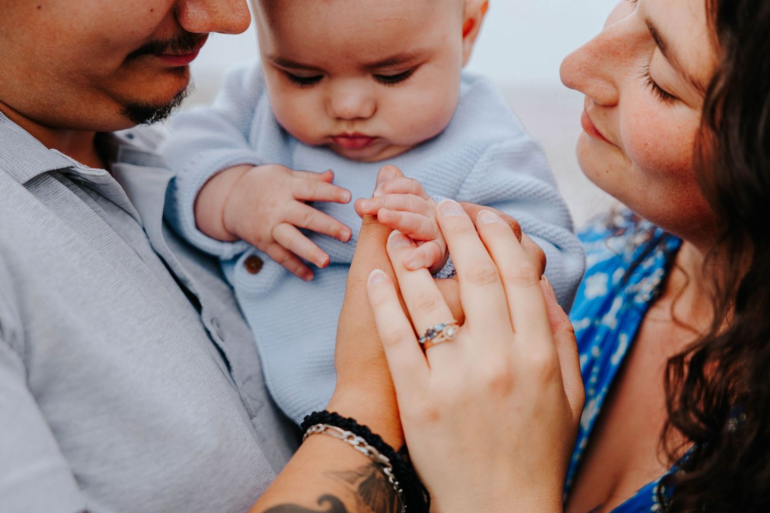 Close-up of parents holding baby with mother showing engagement ring in tender moment.