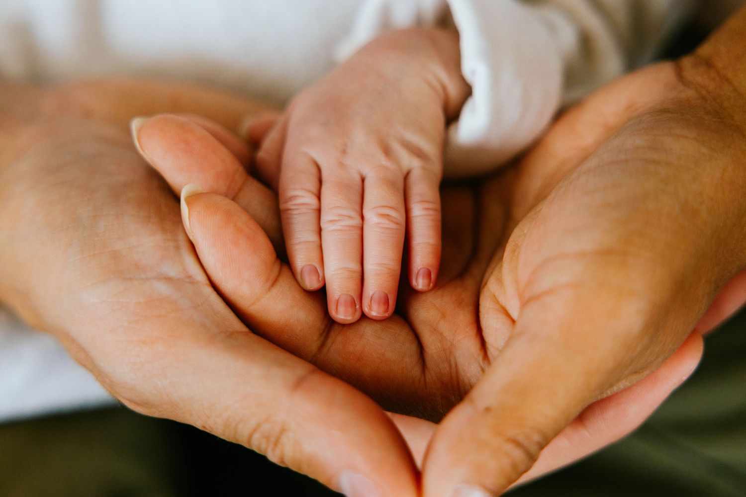 Tiny newborn baby hand rests gently on two large adult cupped hands in a tender close-up.