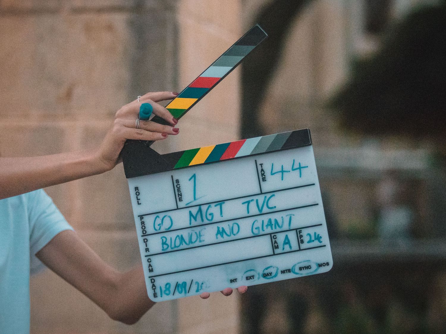 A film slate clapperboard held up by hands against a blurred background.