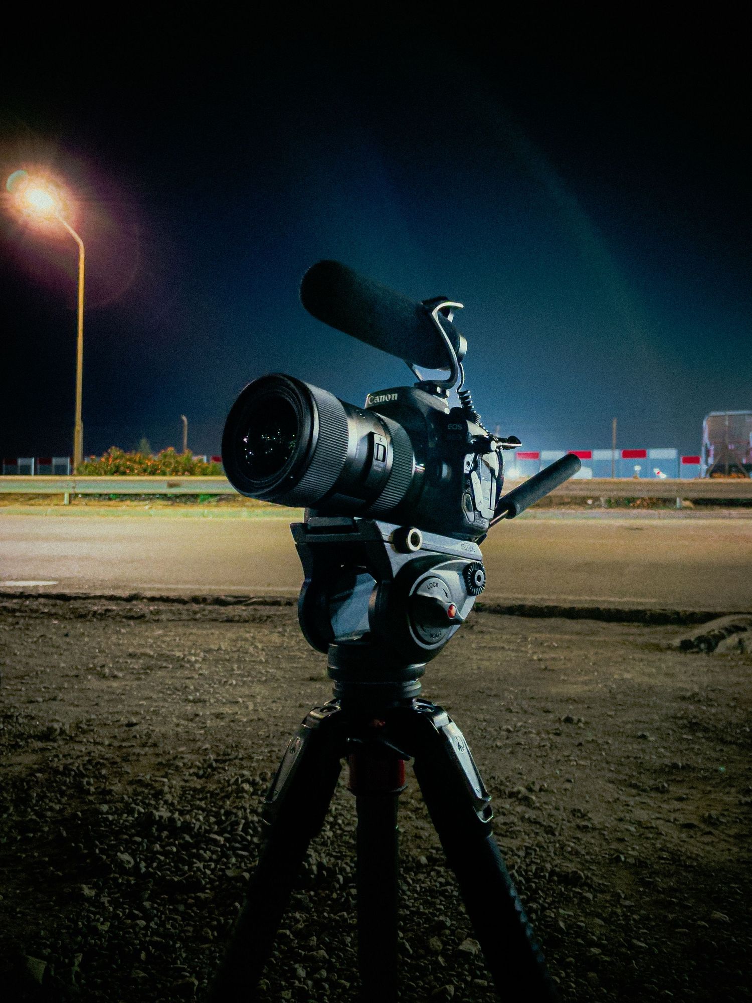 Professional camera setup on tripod at night with street lamp illumination and dark blue sky in background.