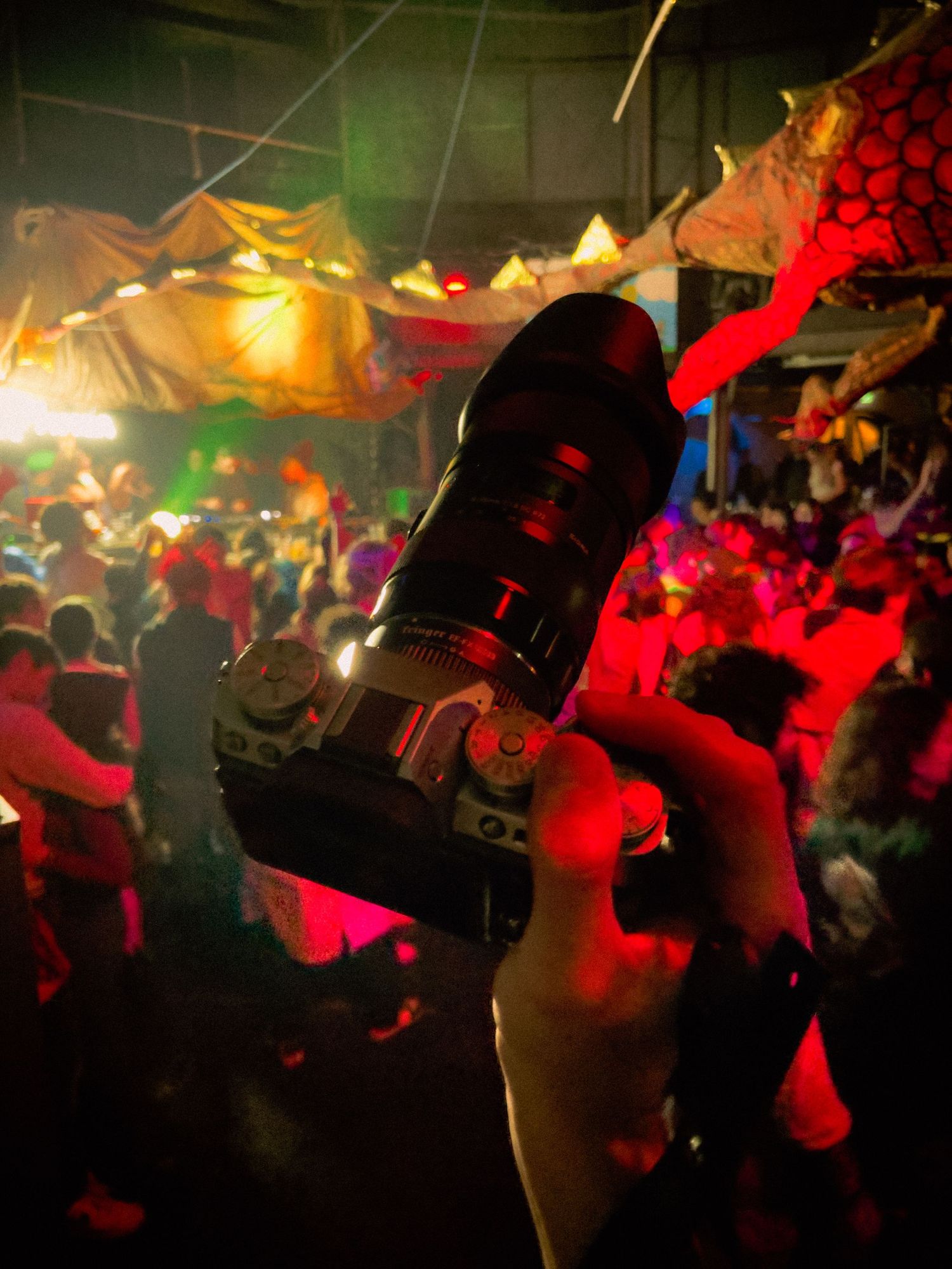 Colorful nightclub scene with a silhouette of a bottle raised high against vibrant red and yellow lighting over a crowded dance floor.