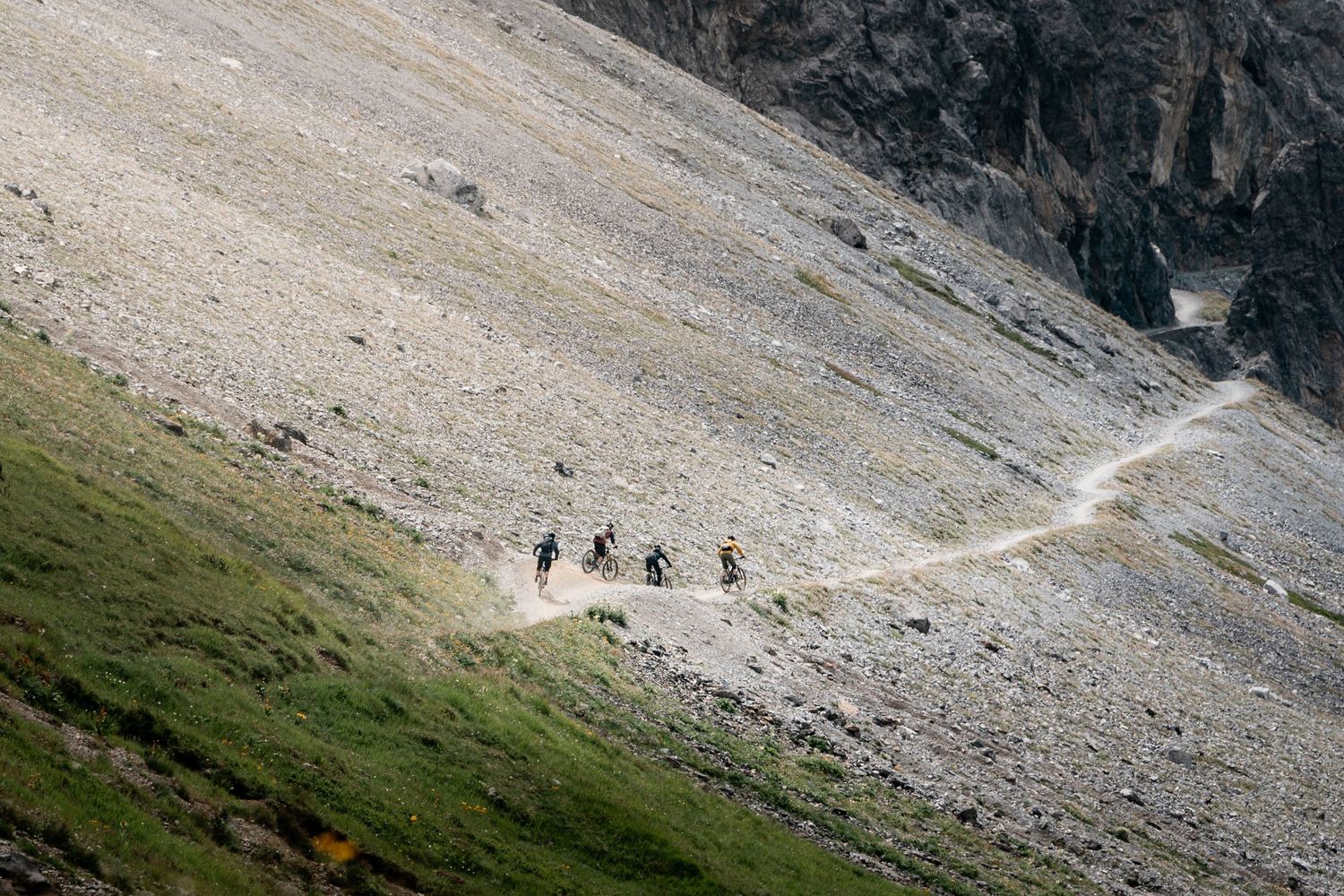 Mountain bikers traverse a rocky mountain trail through rugged alpine terrain.