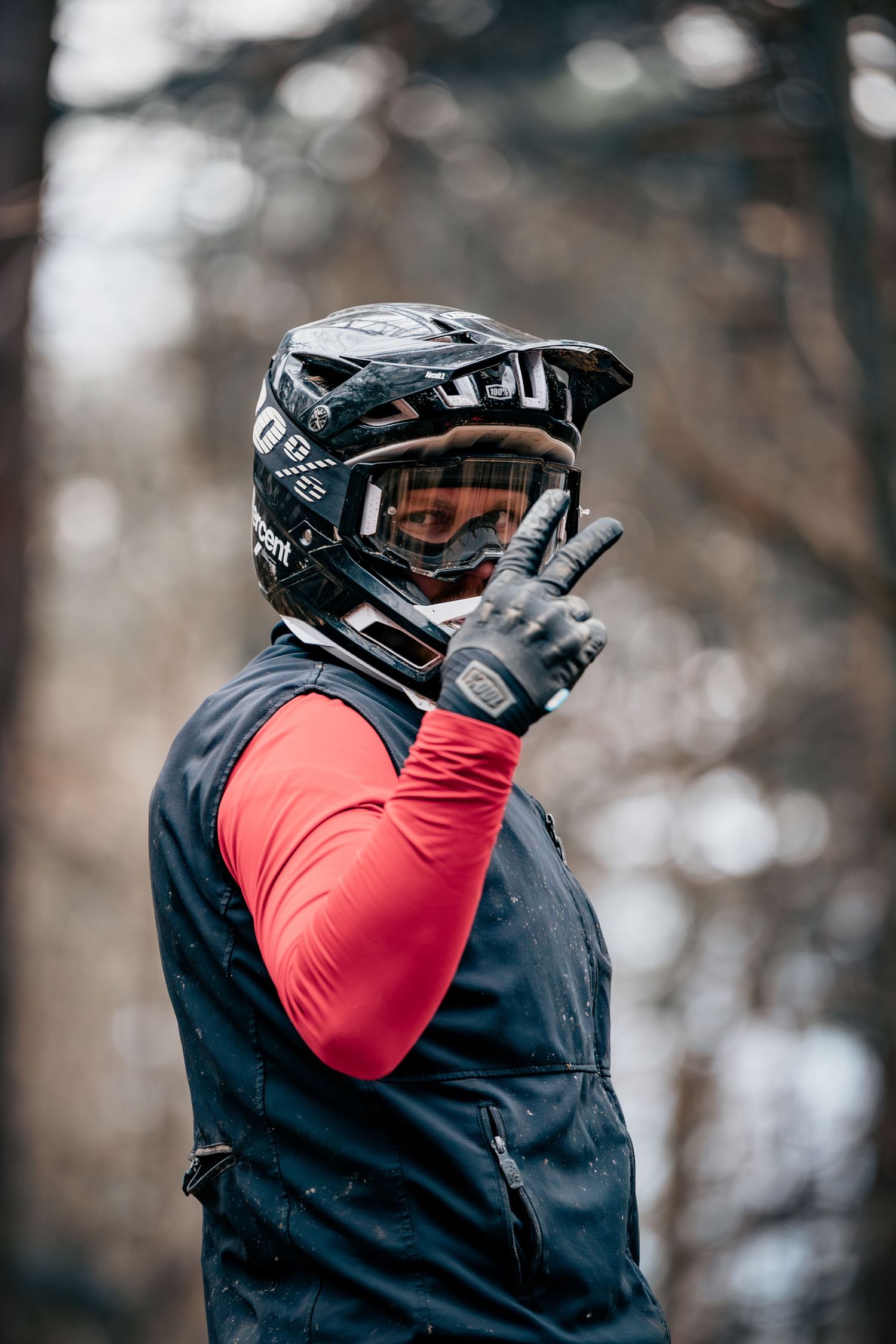 Close-up of mountain biker wearing black helmet and red long sleeve jersey in forest.