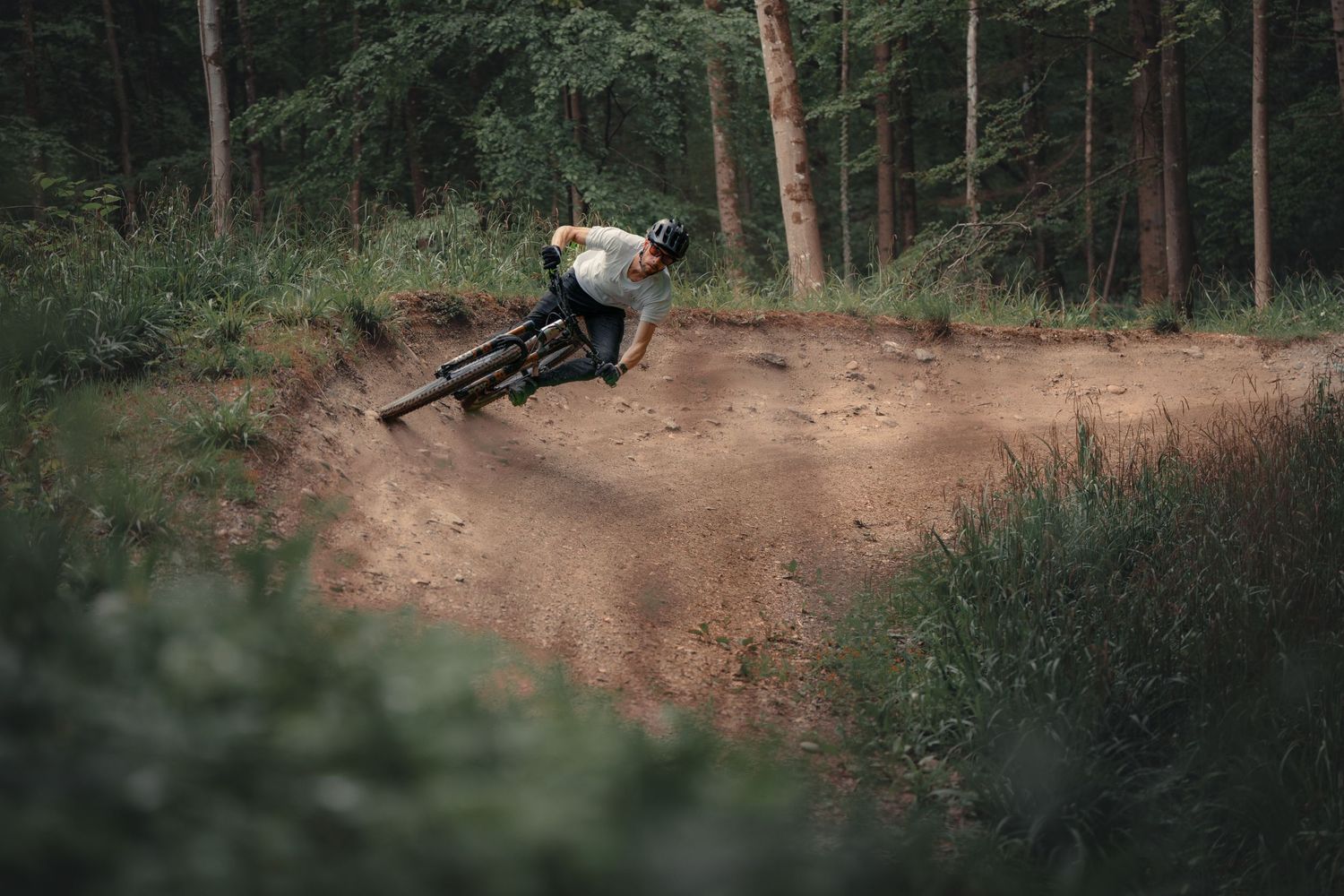 Mountain biker riding through a dusty bermed trail corner in the woods.