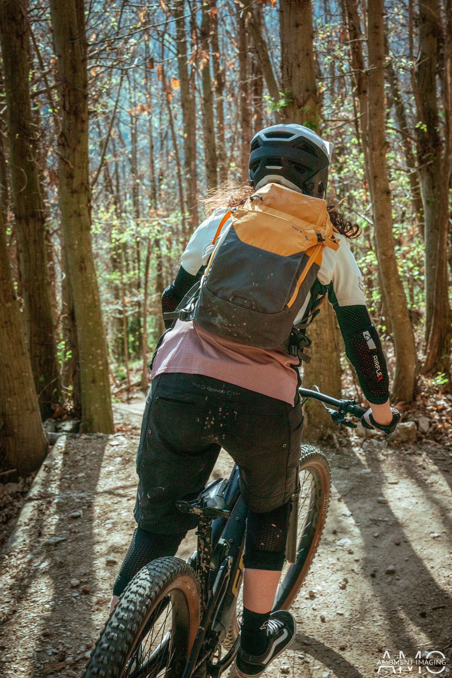 Mountain biker in protective gear and backpack riding through a scenic forest trail.