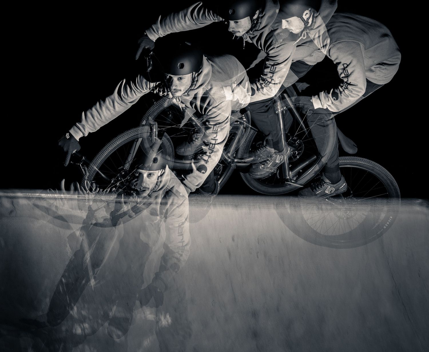 Multiple exposure photo of cyclist in motion creating dramatic ghosting effect against dark background.