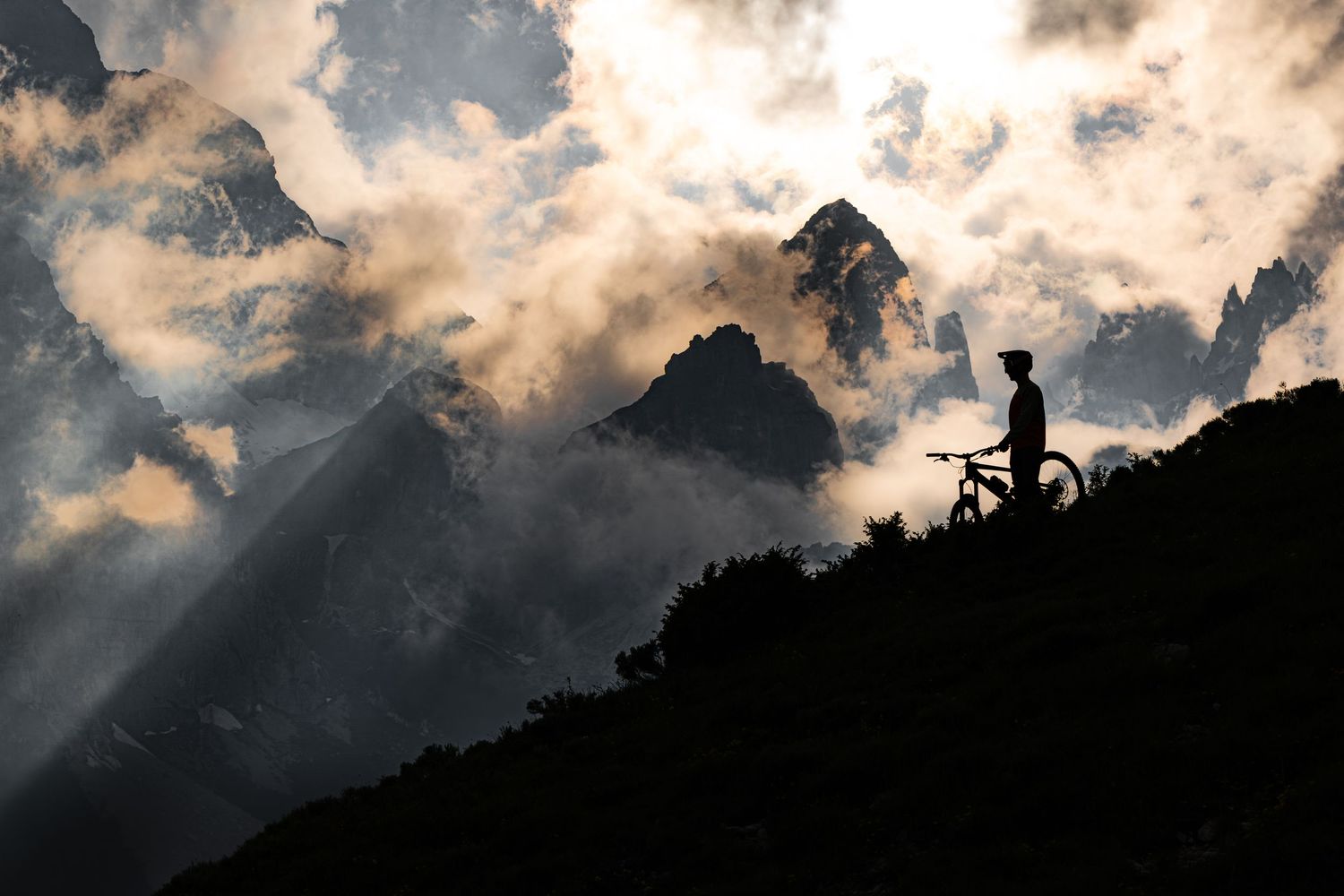 Silhouette of mountain biker against dramatic mountain landscape at sunset.