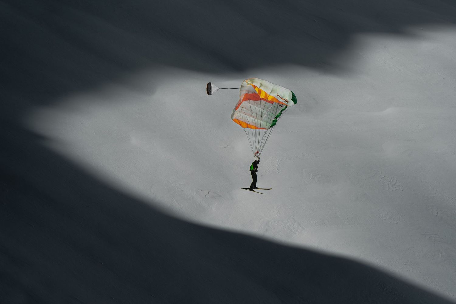 Skydiver with orange parachute silhouetted against dramatic cloudy sky.