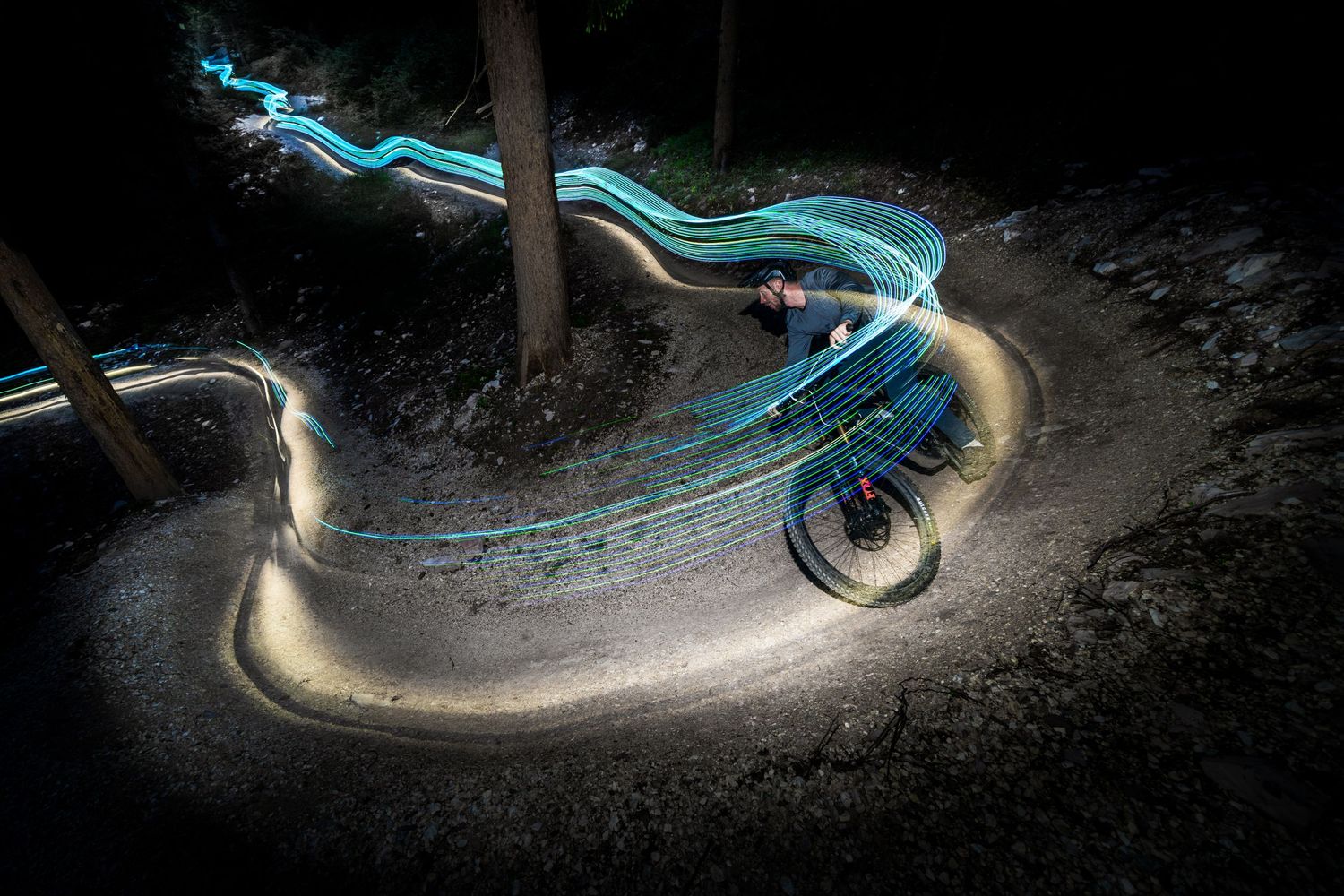 Long exposure night shot of mountain biker creating light trails on a curved dirt trail.