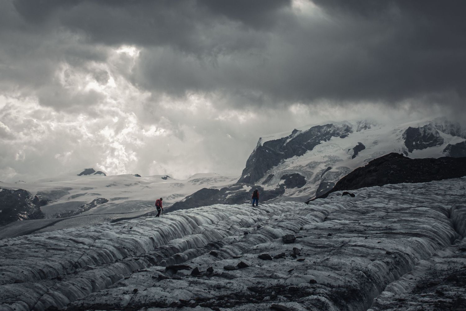 Glacial landscape under stormy skies with mountainous backdrop.