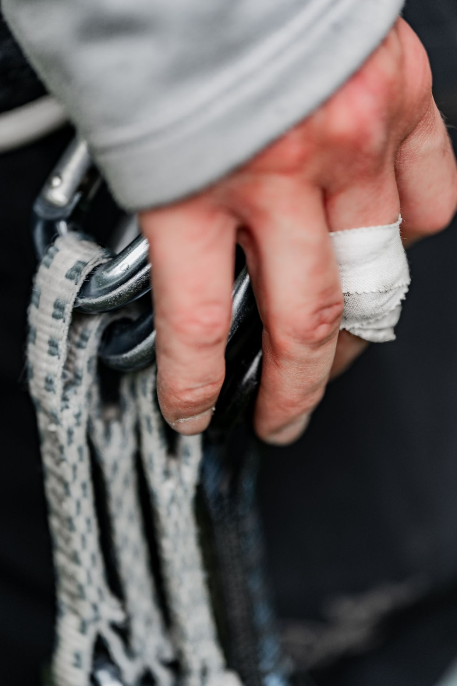 Close-up of climber's taped hand gripping climbing rope against dark background.