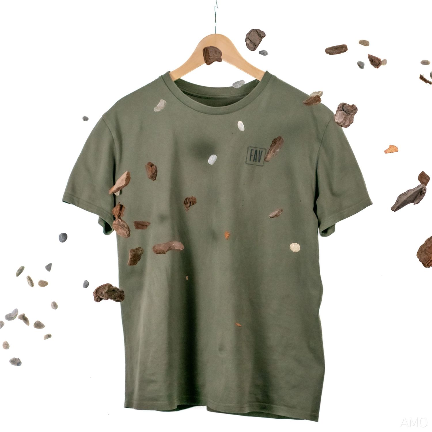 An olive green t-shirt displayed with scattered brown abstract elements floating around it.