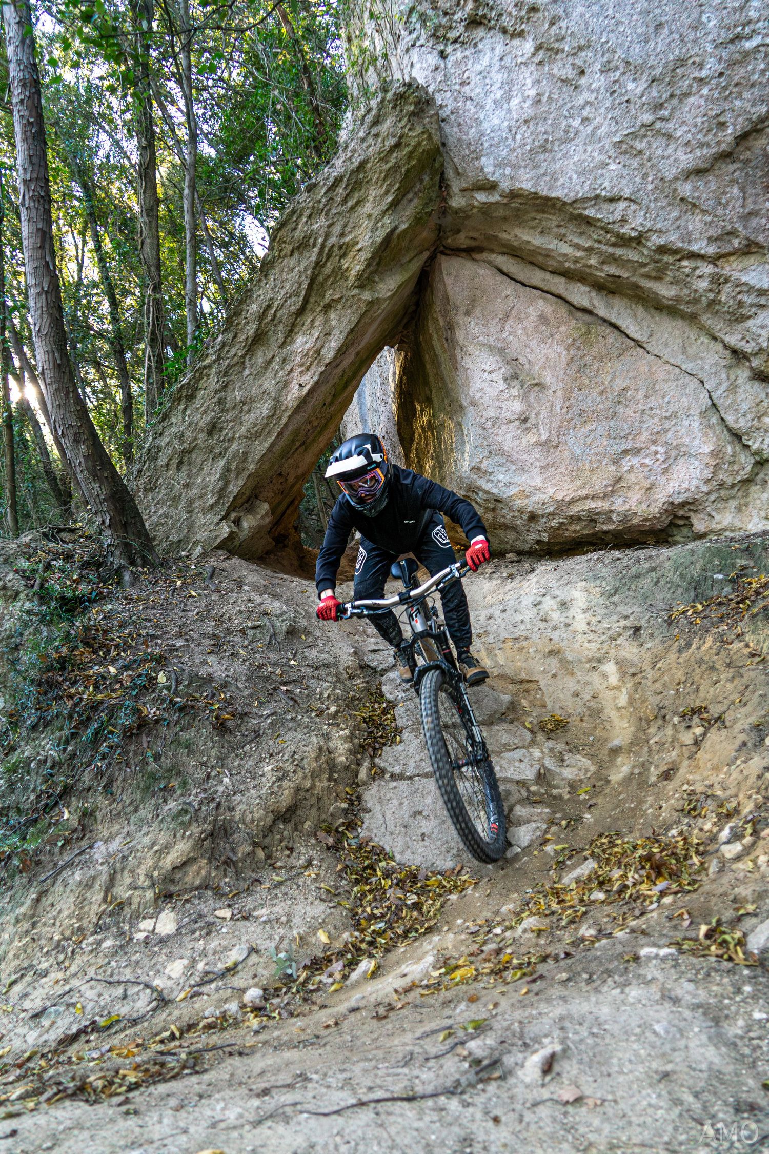 Mountain biker navigates a steep rocky section beneath a natural stone arch.