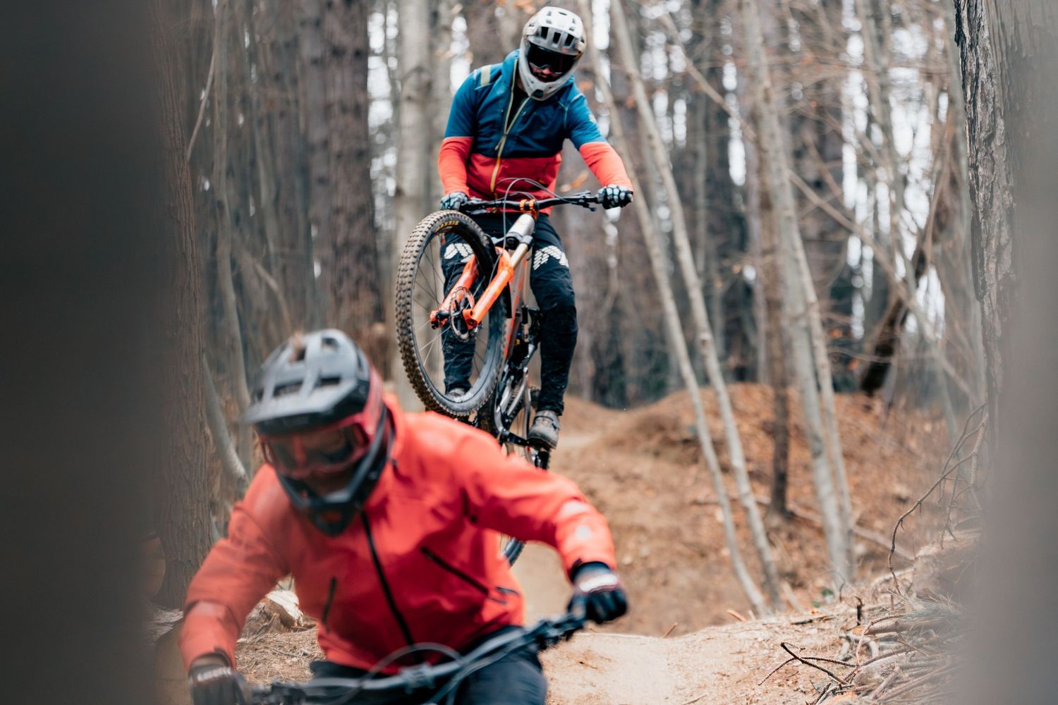 Two mountain bikers racing through wooded trail with dynamic action.