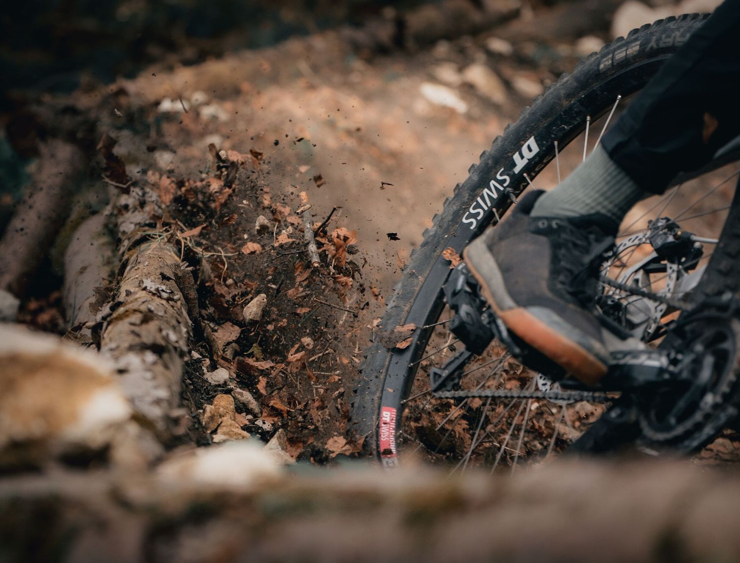 Close-up shot of a mountain bike tire kicking up dirt and debris on a muddy trail during off-road cycling.