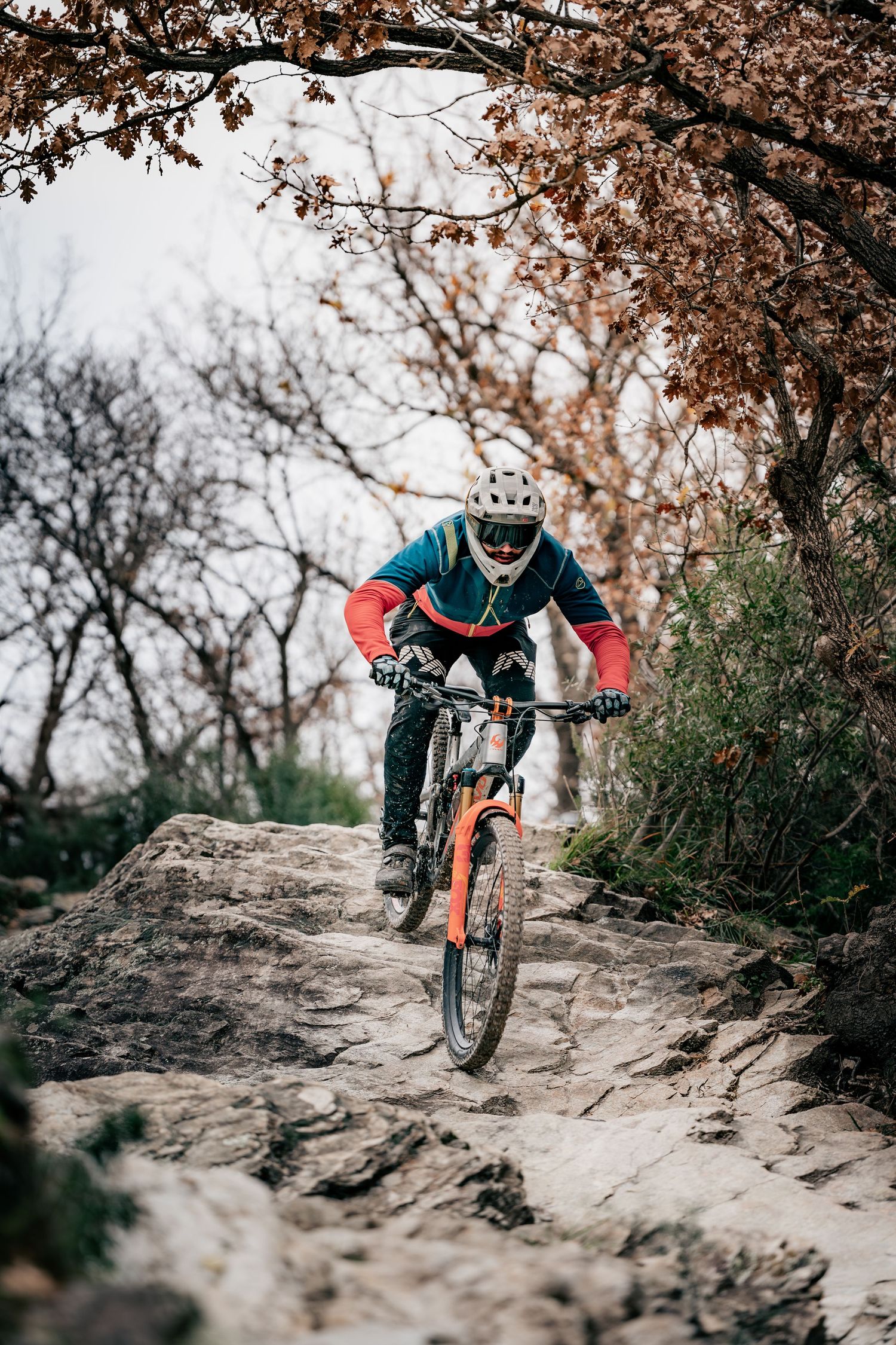 Mountain biker riding rocky trail beneath autumn trees with skilled technique.