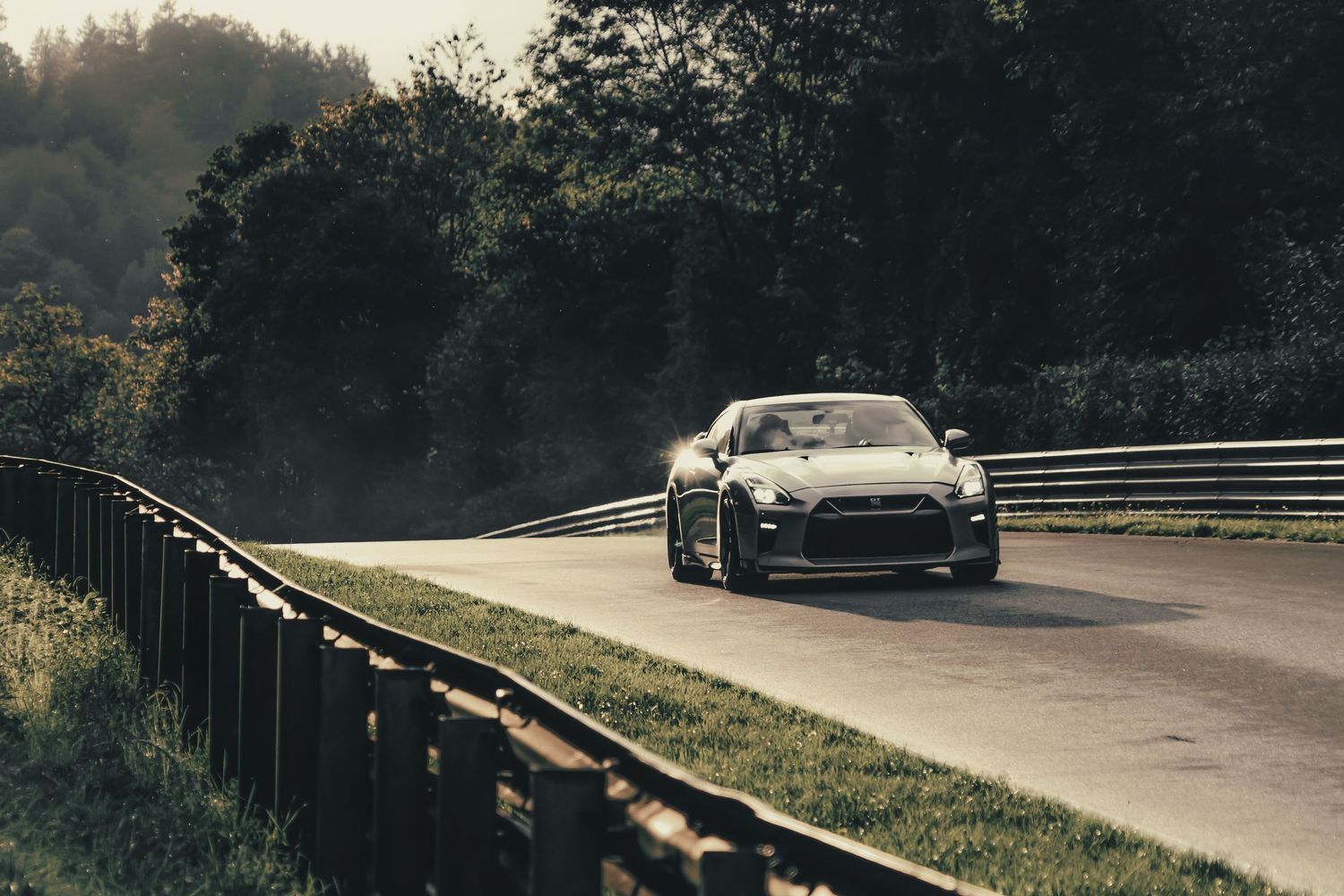 A sleek sports car navigates a curved road through forested scenery, kicking up tire smoke.