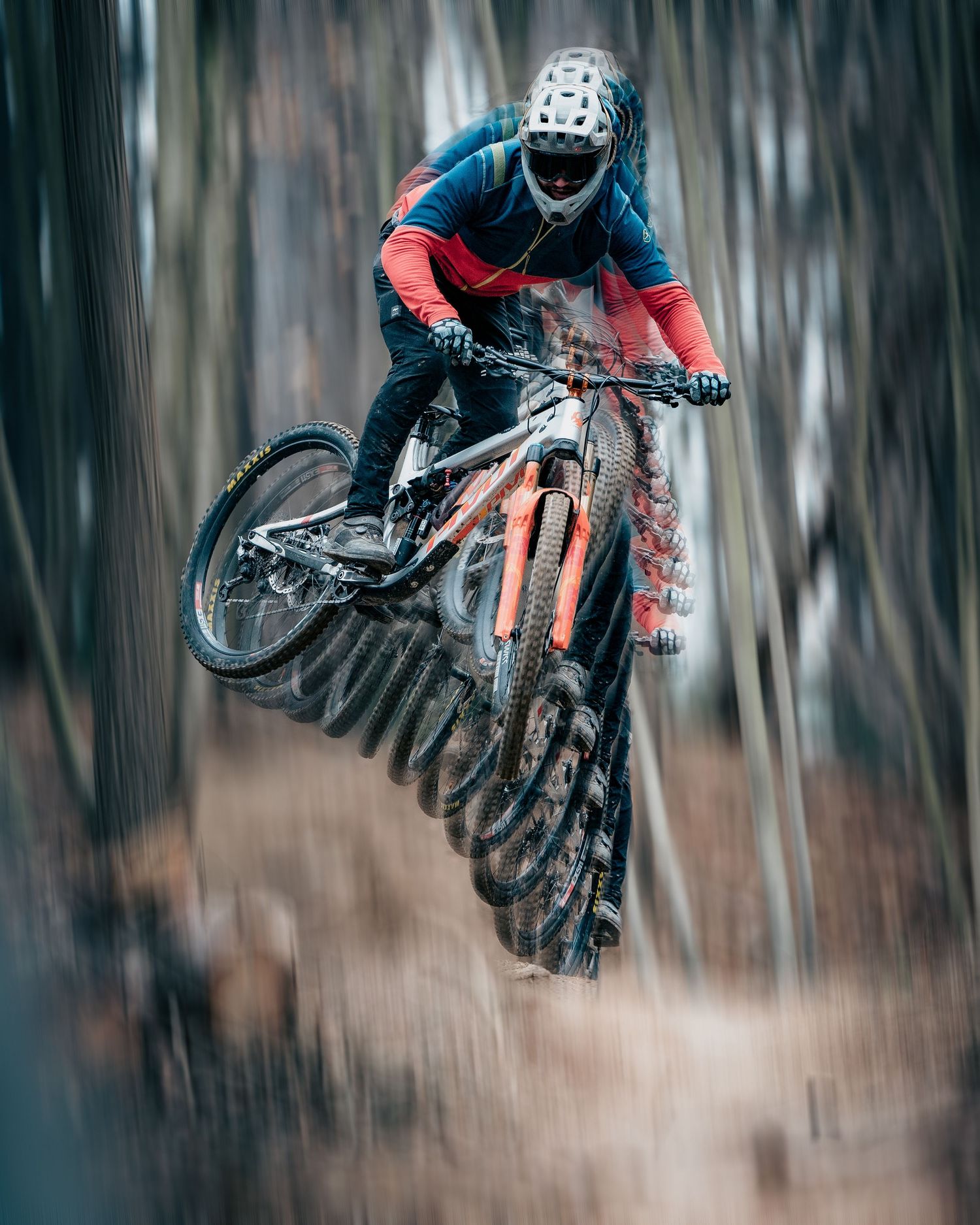 Mountain biker performs impressive jump with bike in mid-air through forest with motion blur effect.