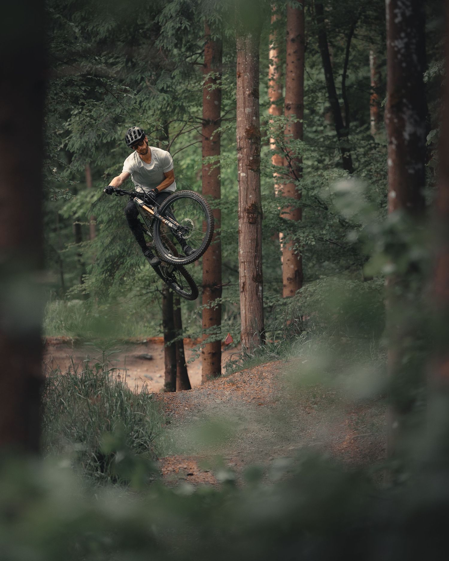 Mountain biker performing a high jump between trees in a misty forest setting.