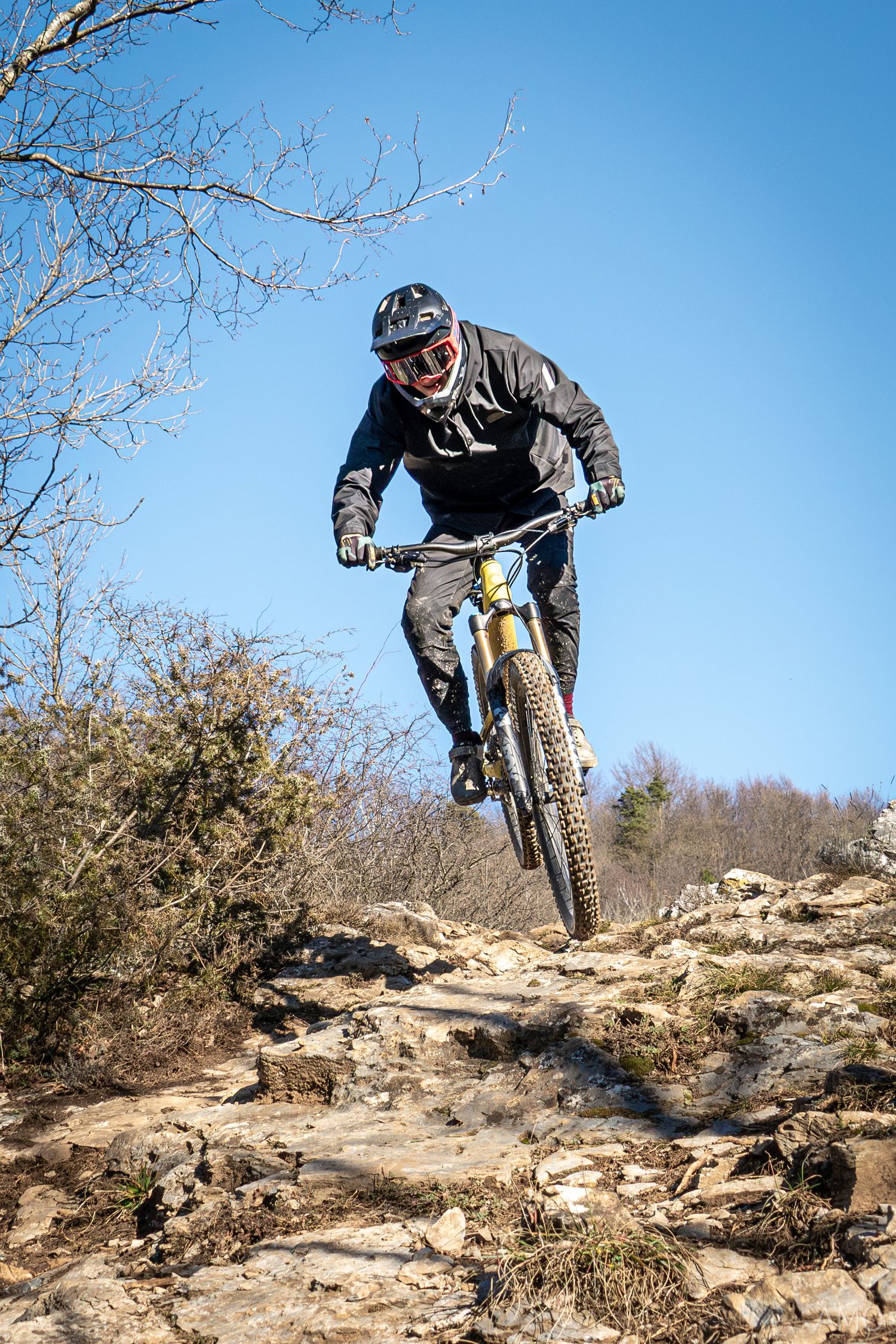 Mountain biker jumping off rocky terrain against clear blue sky background.
